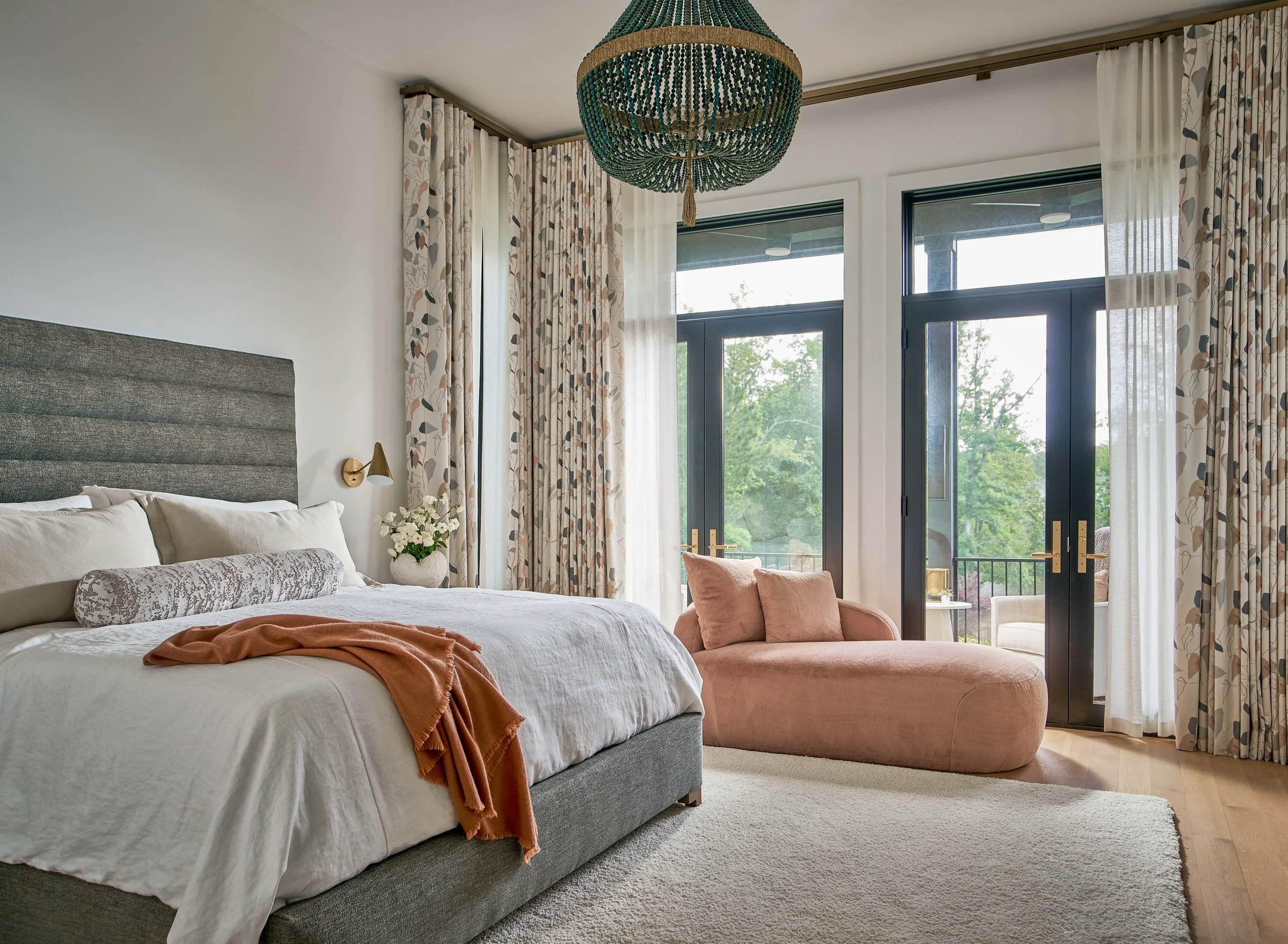 primary bedroom design with tall ceilings chandelier upholstered headboard chaise lounge and double french doors leading to a private balcony by cat french design durham interior designer chapel hill interior designer luxury interior designer nc