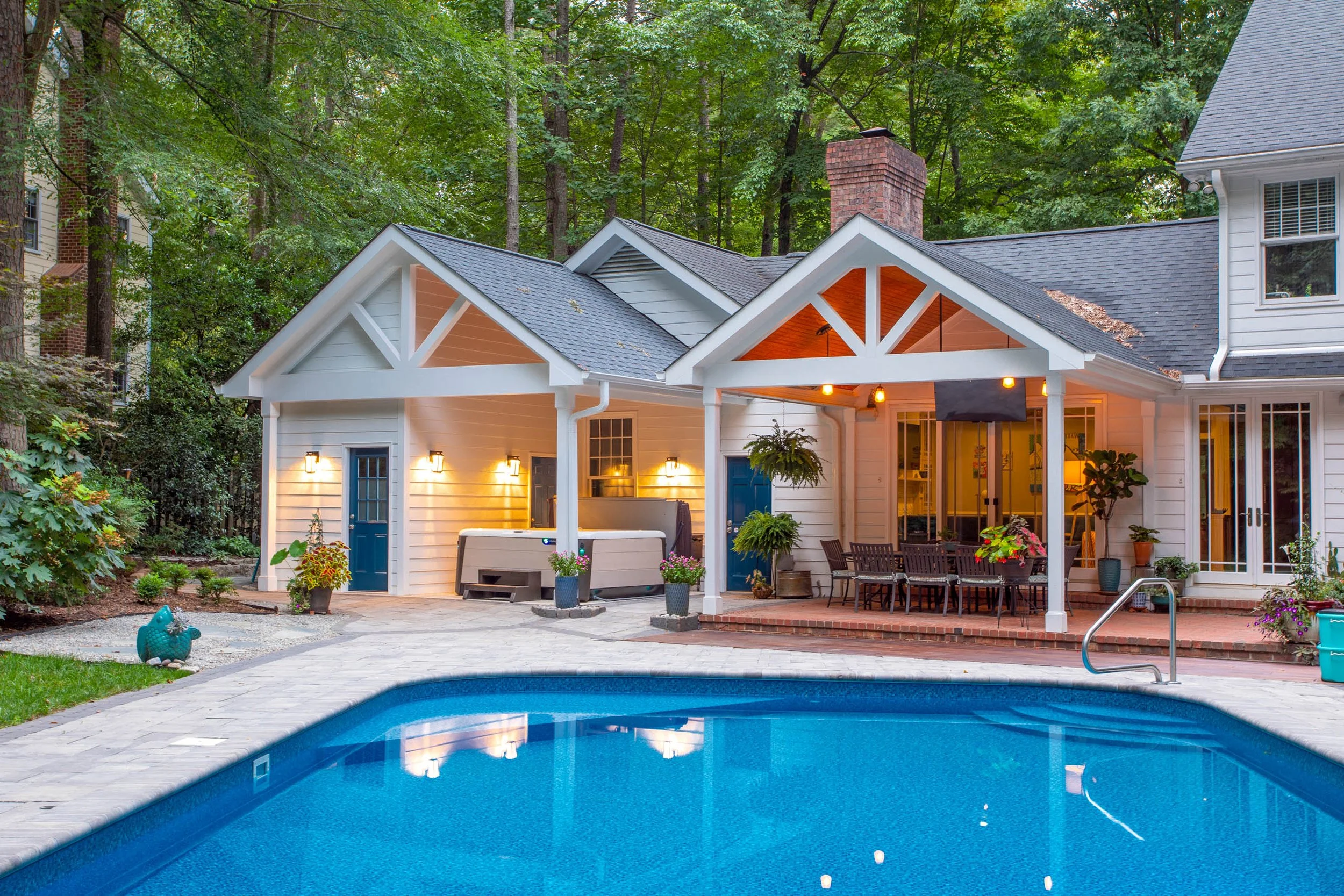 view of a house with white siding and gabled roof with pool brick patio outdoor dining area hot tub and blue doors leading to pool house bathroom addition
