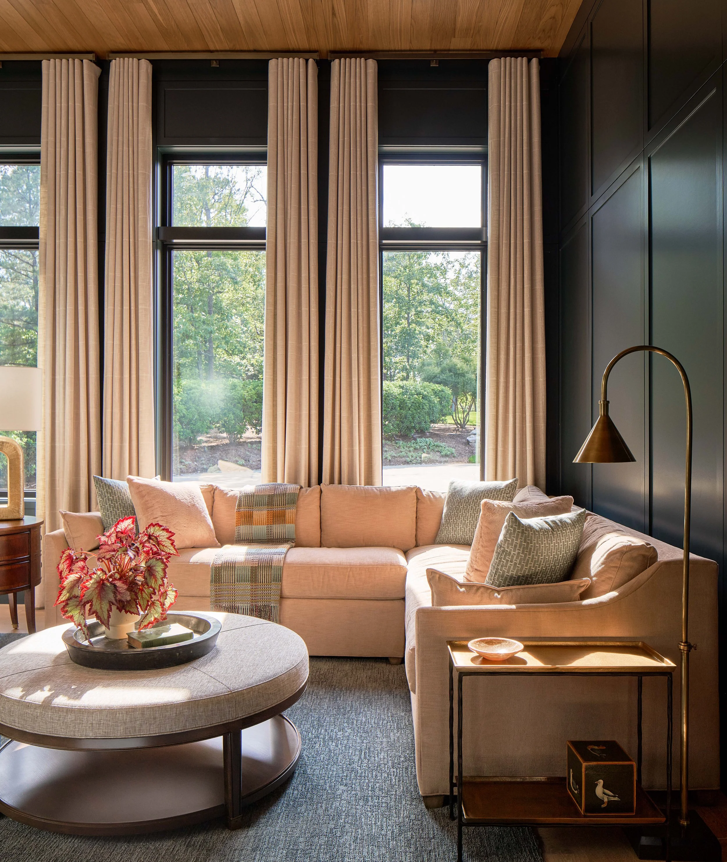 a cozy family den with dark blue walls and inlaid wood ceiling corner sectional couch and upholstered coffee table family friendly luxury design by cat french design durham interior designer chapel hill interior designer