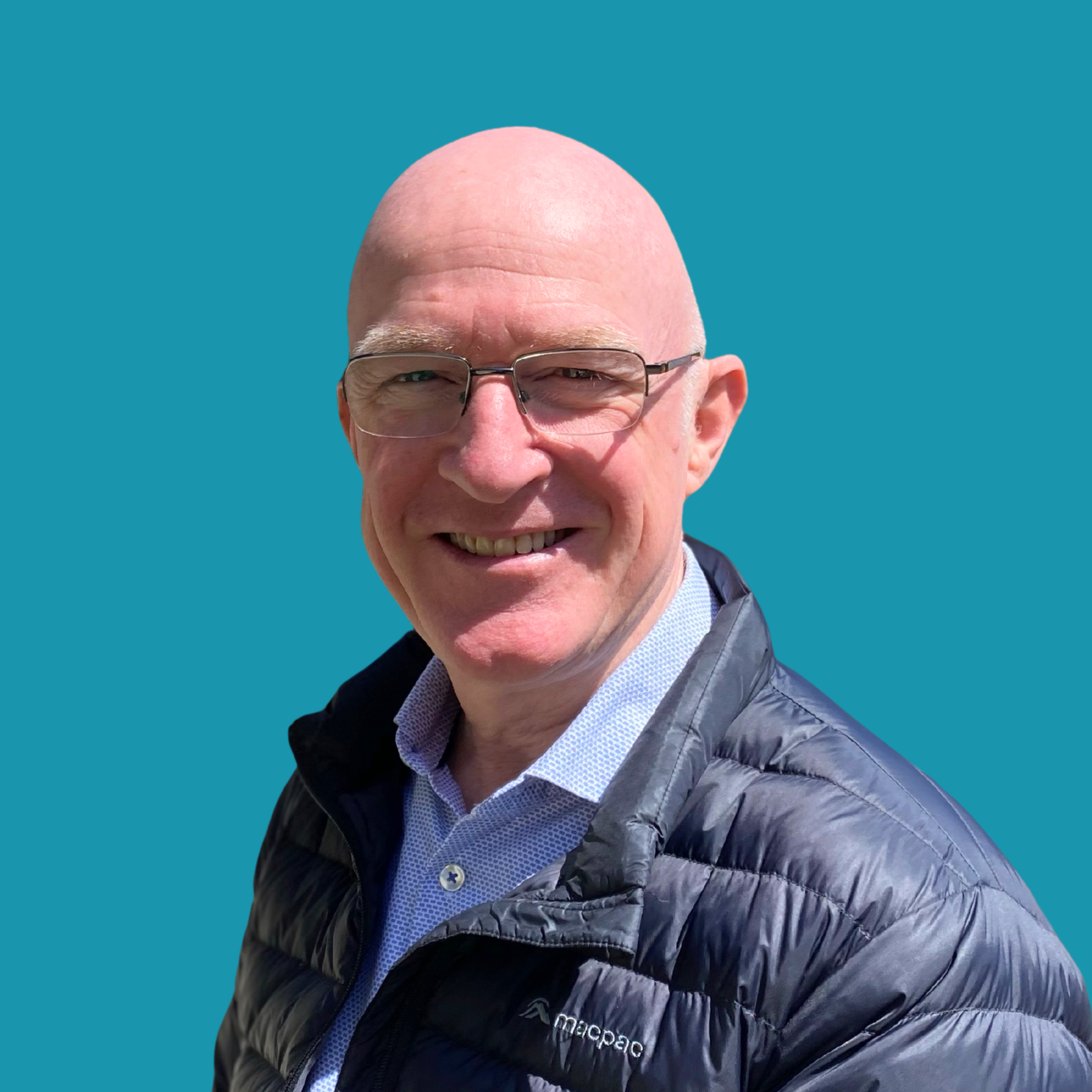 Headshot of male with no hair and with blue jacket on teal background