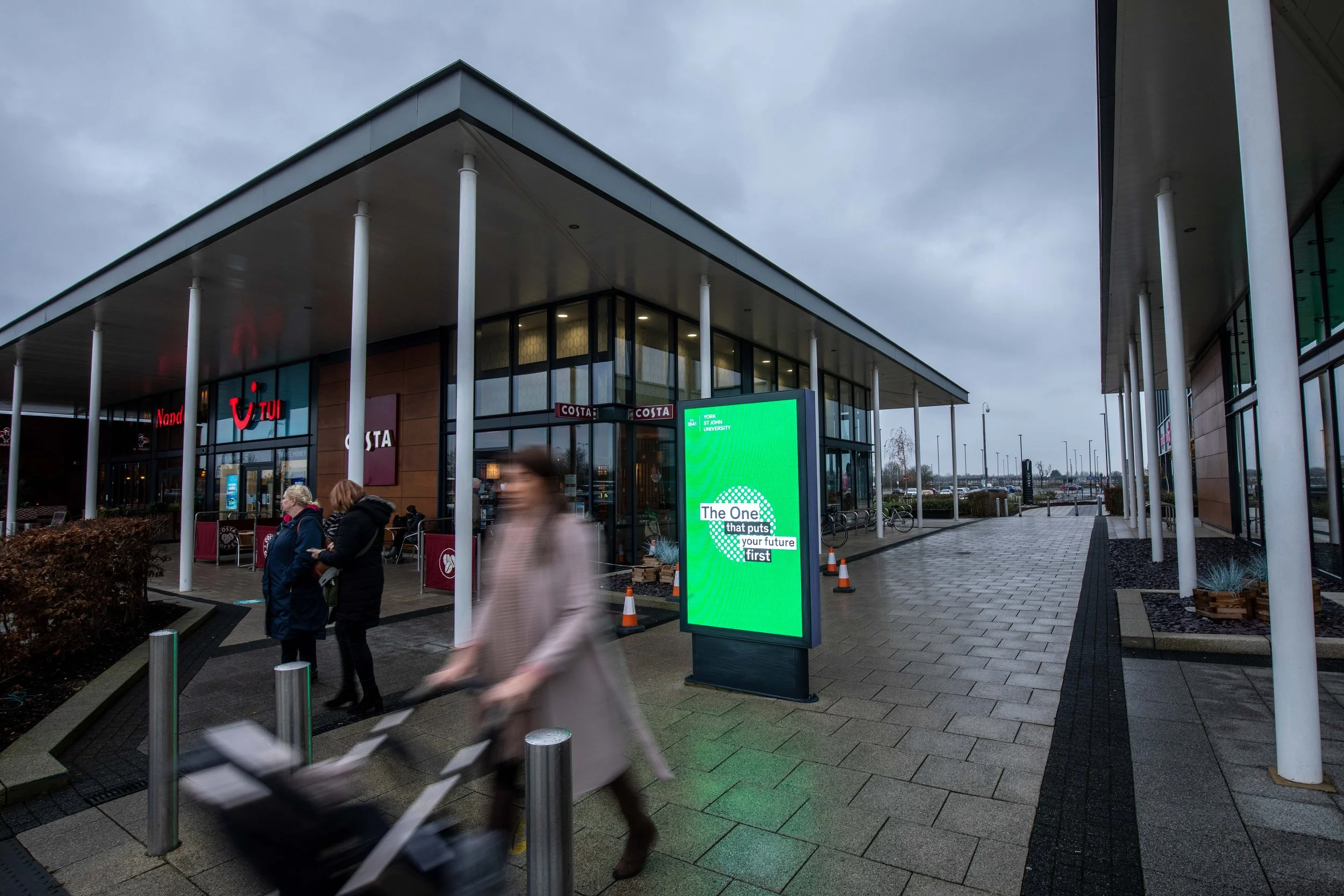 People walking past an outdoor advertising screen in shopping centre