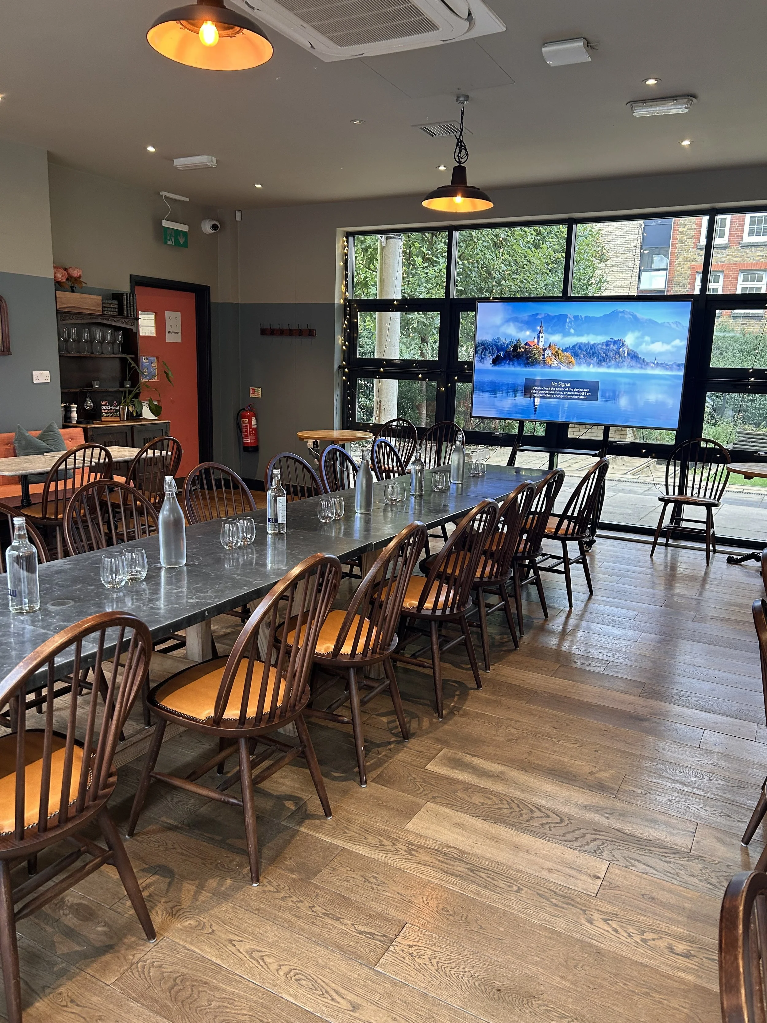 Our area for private meetings, a long table set with glasses and water bottles, a large window with a TV screen, and wooden chairs.