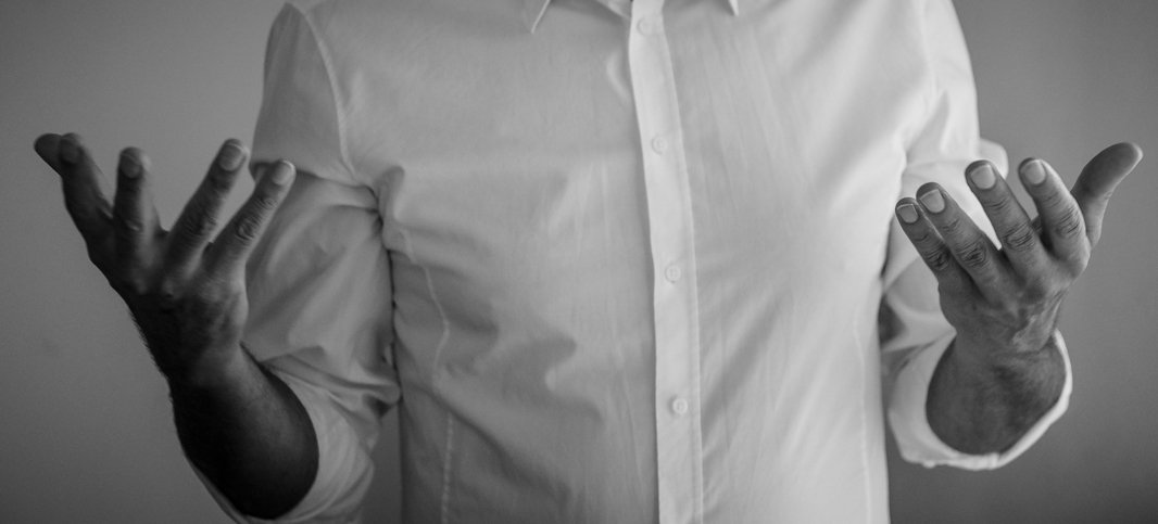 Person in einem weißen Hemd gestikuliert mit beiden Händen erhoben, schwarz-weiß Foto.