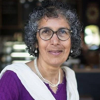 Smiling woman with curly gray hair and glasses outdoors
