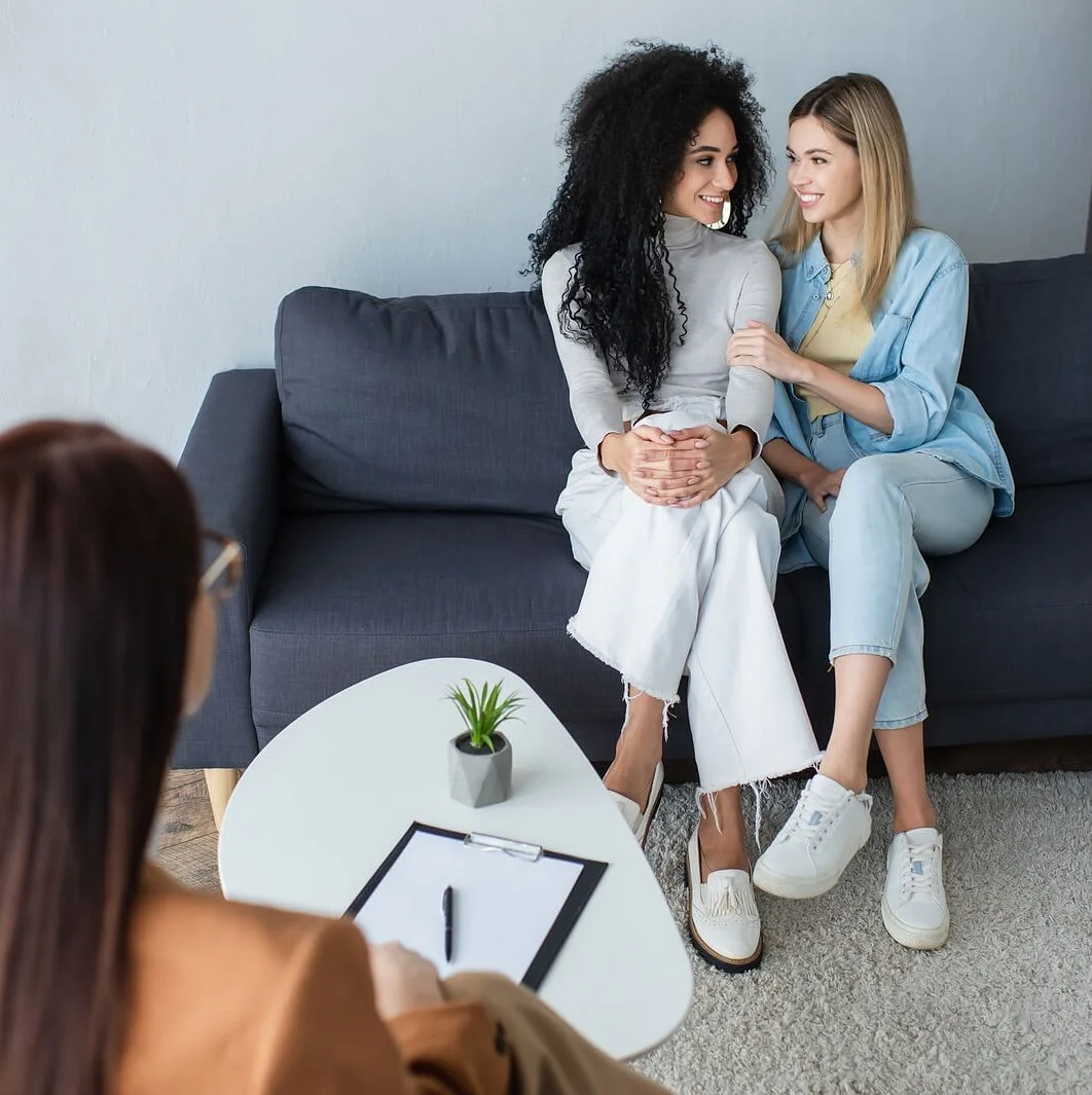 A couple sitting close on a couch while speaking with a therapist