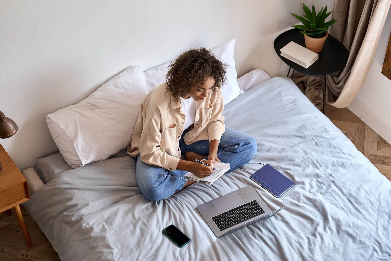 A young woman sitting in bed writing in a notebook