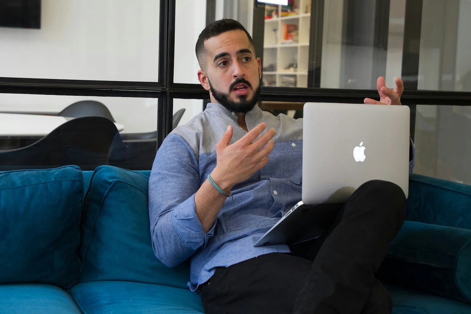 A man sits on a couch with his laptop in a meeting