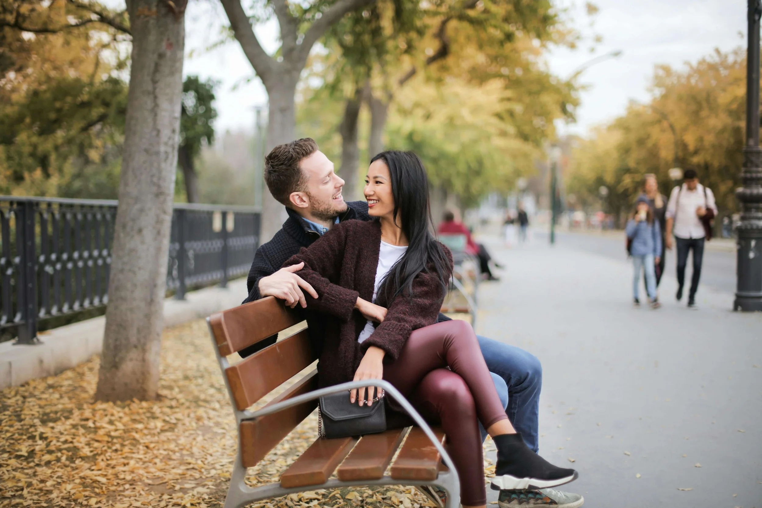 A couple sitting on a park bench smiling at each other