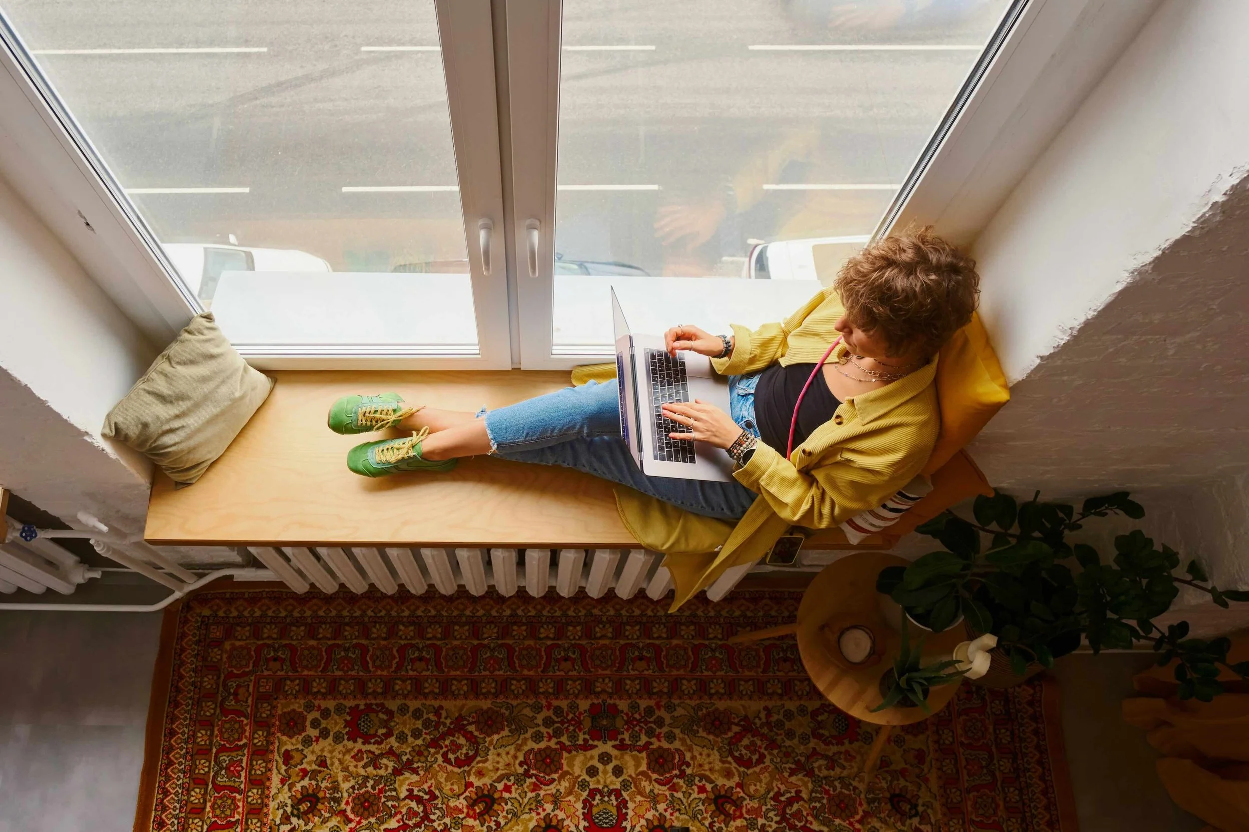 A woman sitting on a window seat with a laptop on her lap
