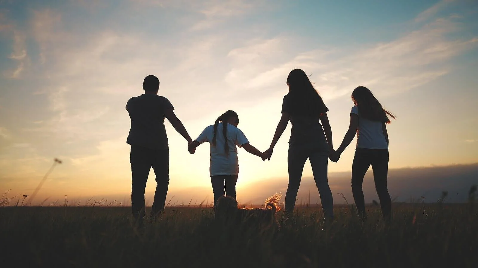 A family of four walking in a field with a dog