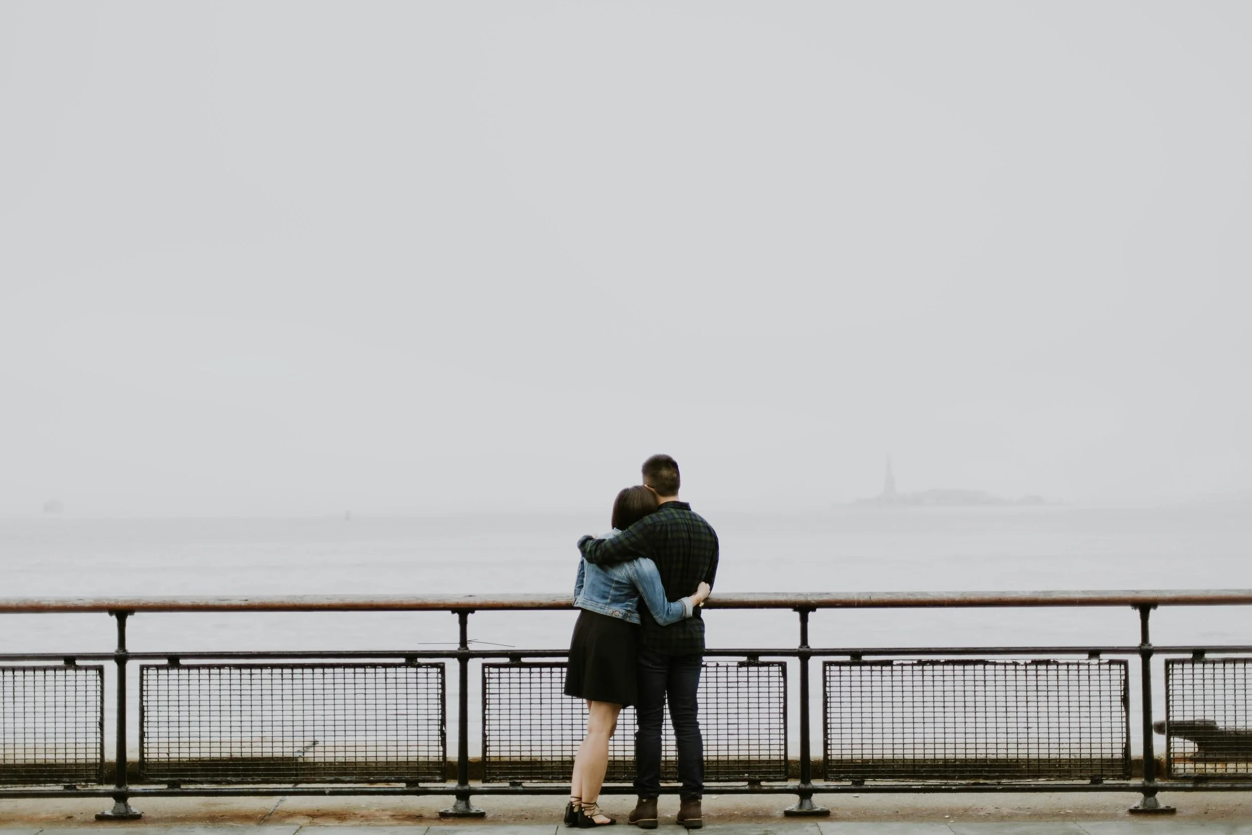 Couple hugs while looking through fog at Statue of Liberty