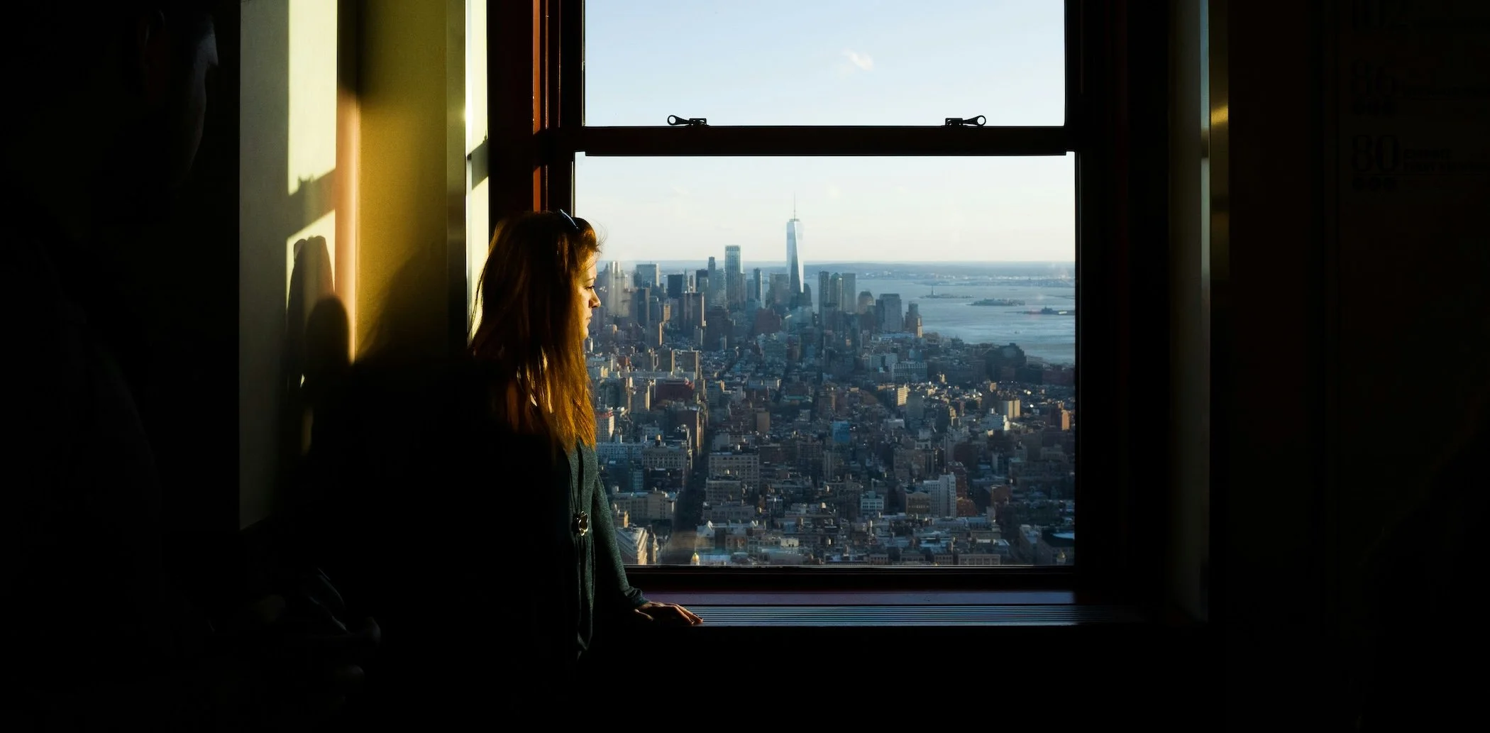 Woman looks out window to NYC skyline.