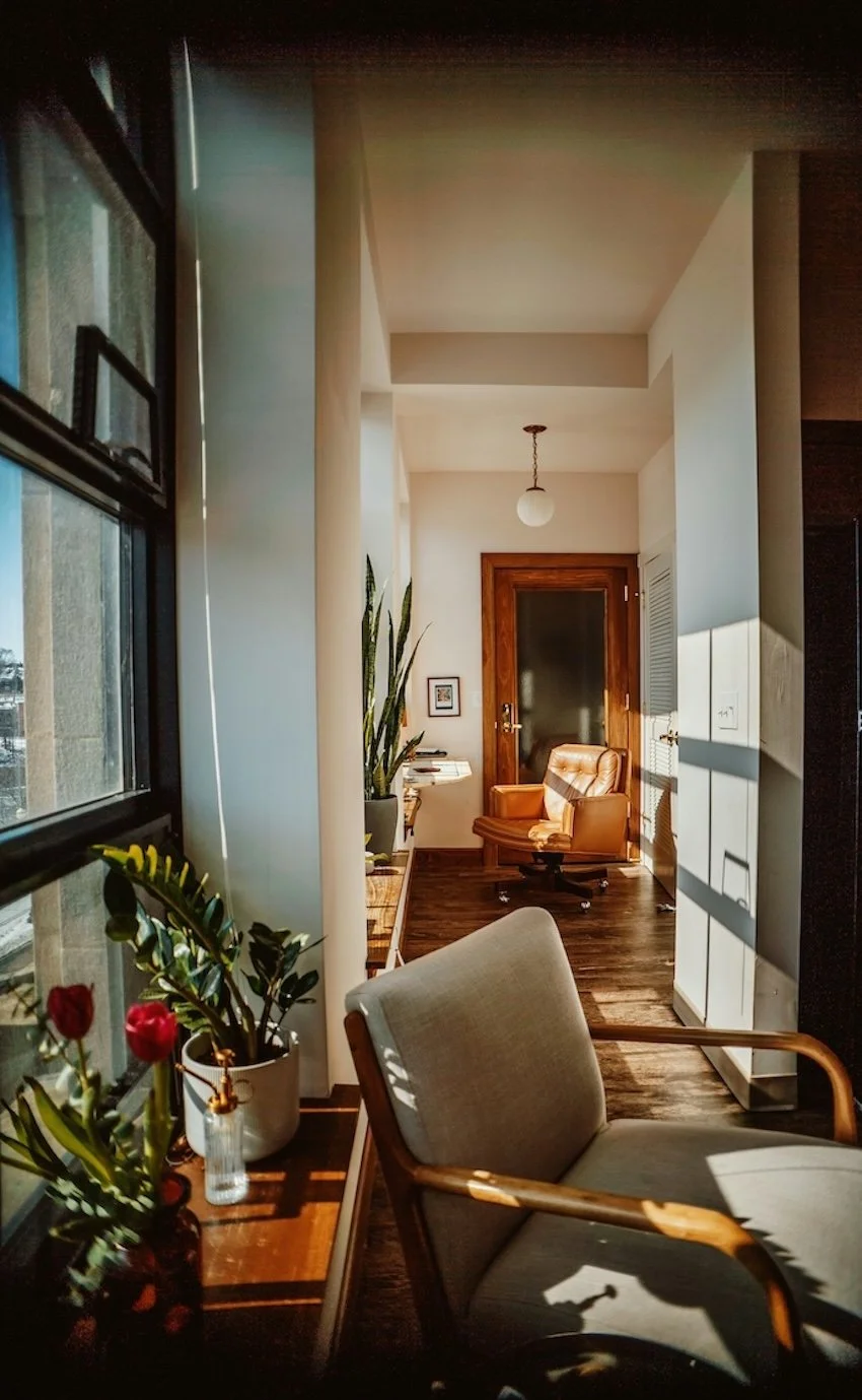 A sunlit therapy office with two chairs, plants, and warm natural light