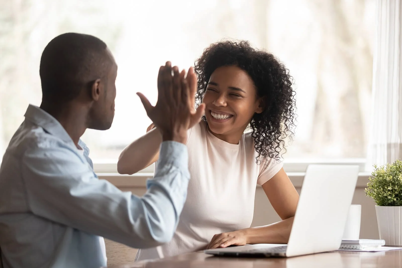 A couple high-fiving over a laptop at a table