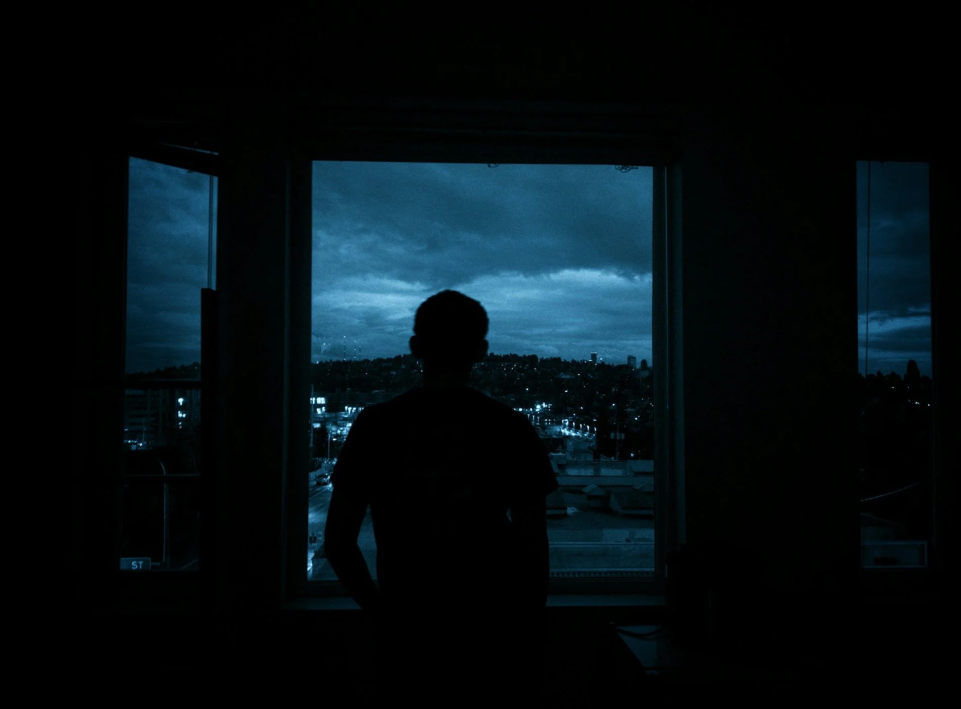 Dark silhouette of a person looking out at a city through a window.