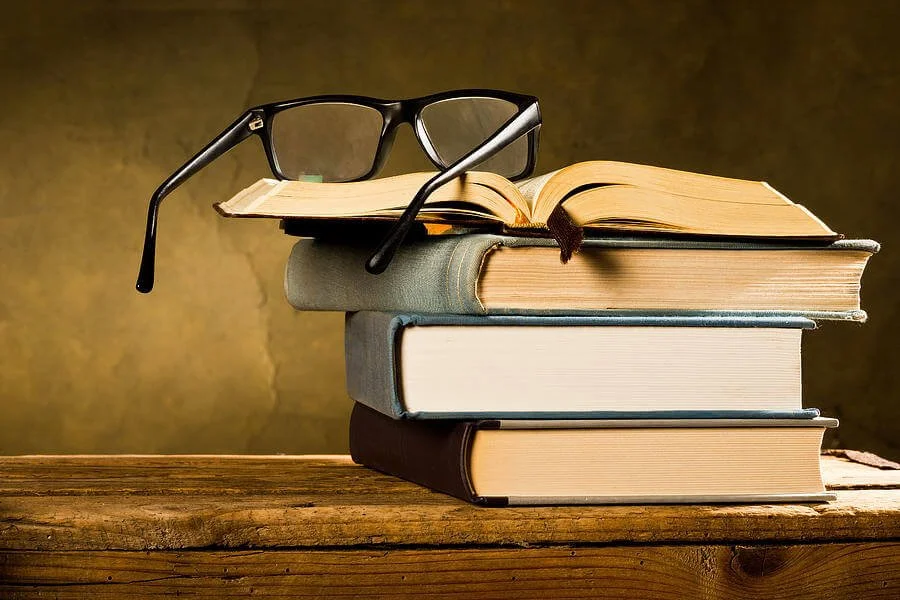 A stack of books with a pair of glasses resting on top