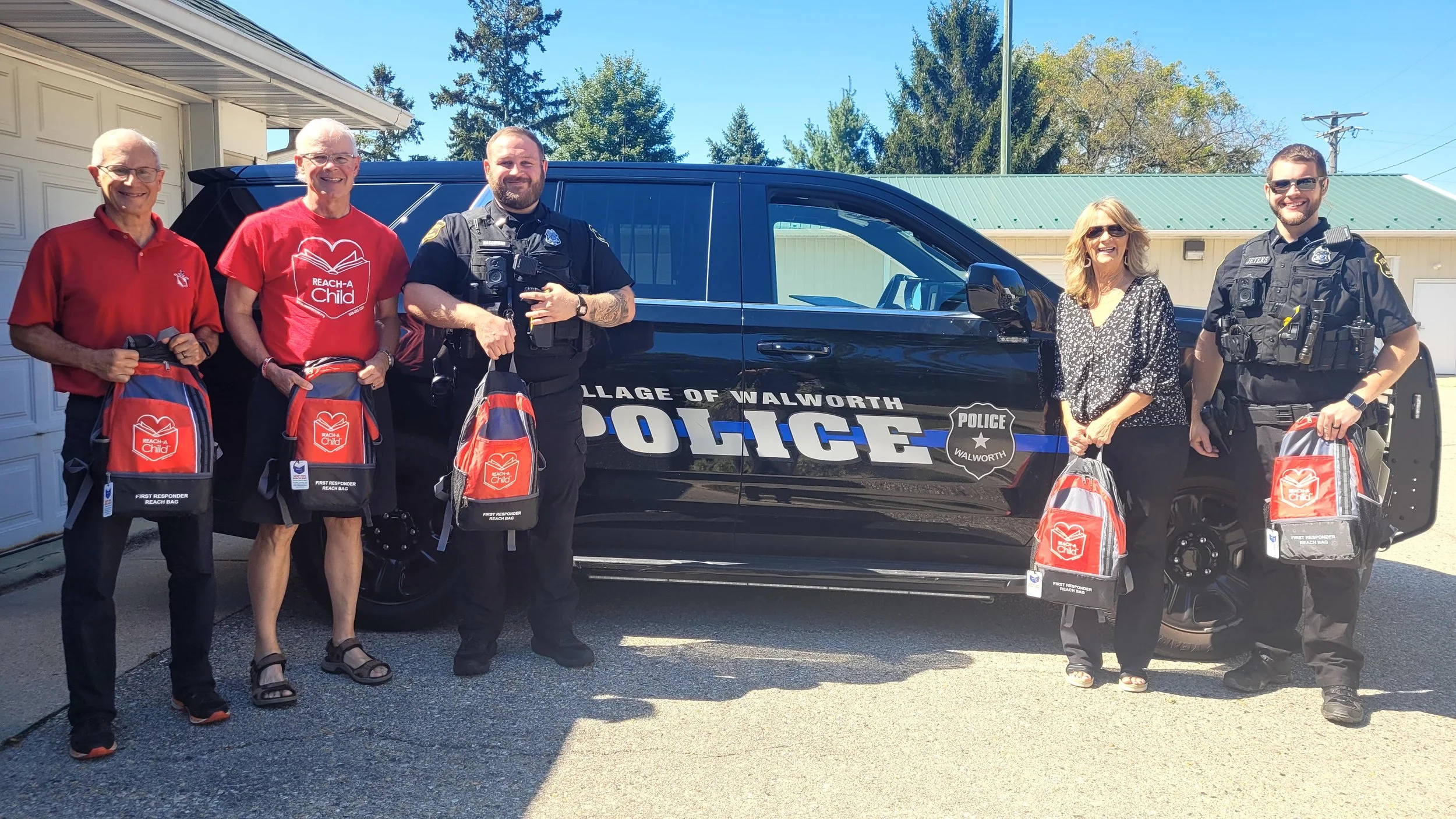 REACH-A-CHILD with REACH BAGs shown with the Village of Walworth Police Department officers in front of a police car