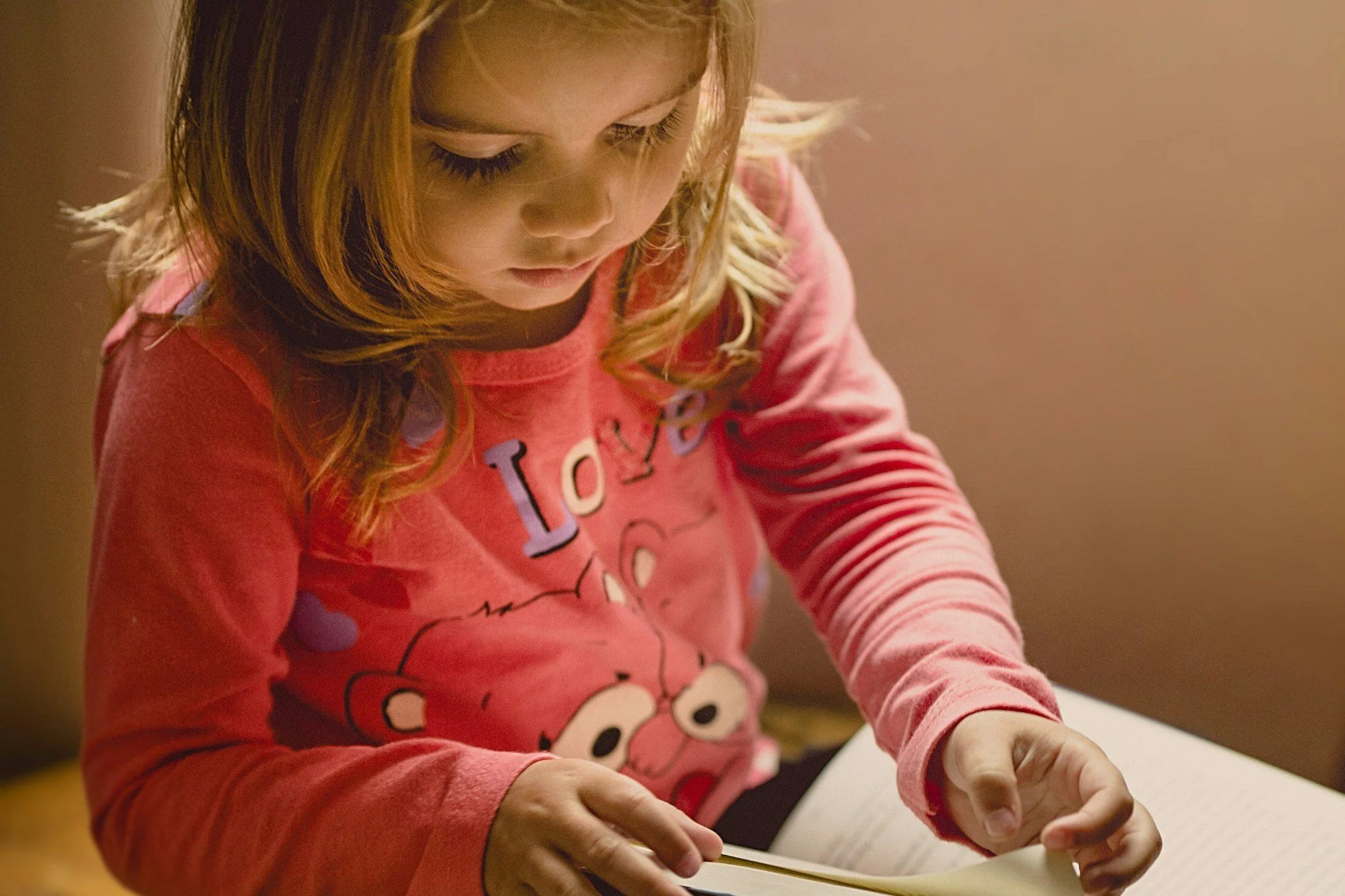 Young child in a pink shirt reading a book indoors.