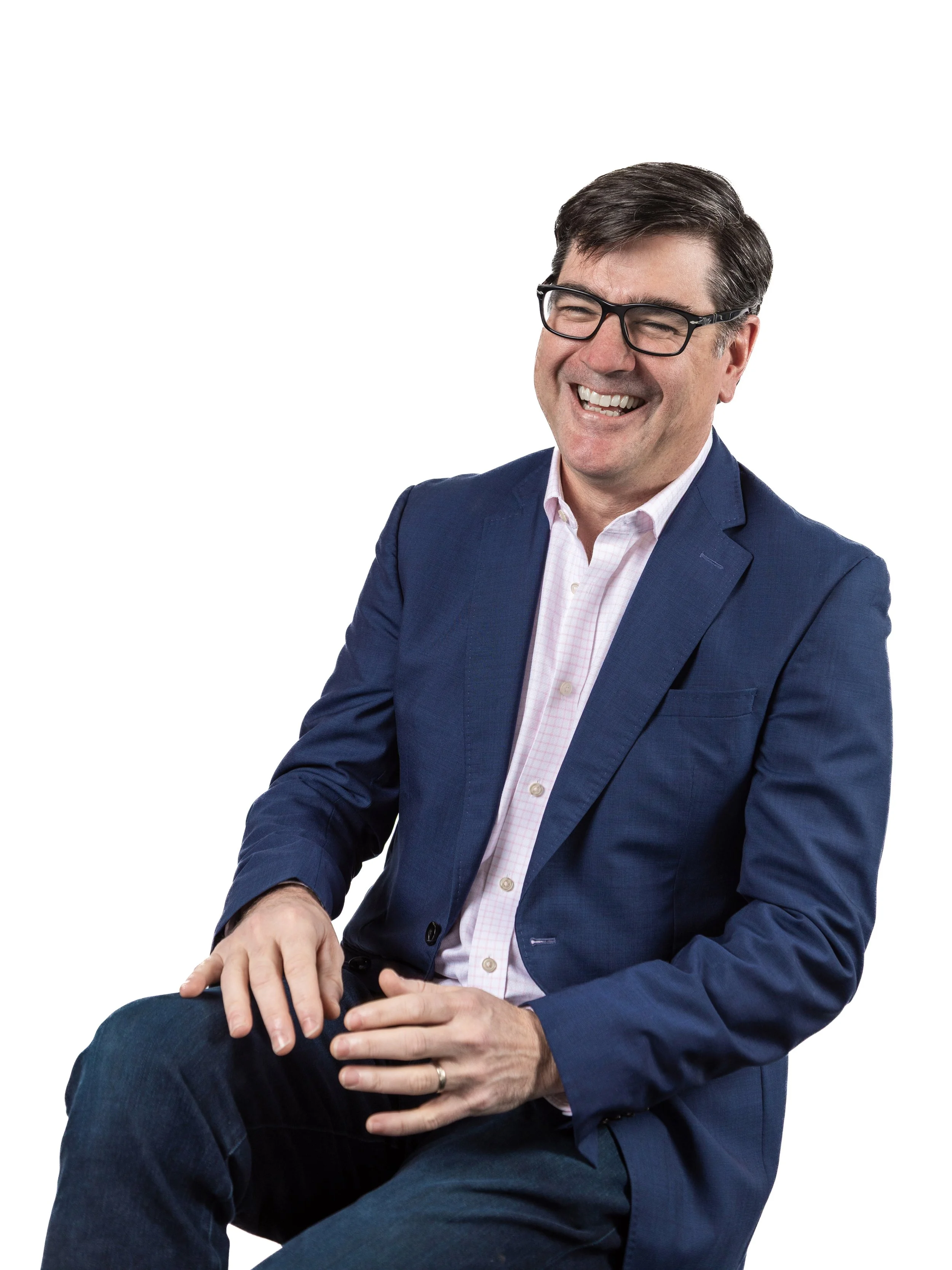 Half body photo of chief client officer Michael Chapman sitting in a both at Lopposum, a fine french restaurant in Richmond, Virginia. Artwork of a clown mysteriously holding a knife is on the wall behind him. Michael is wearing a pink button-down.