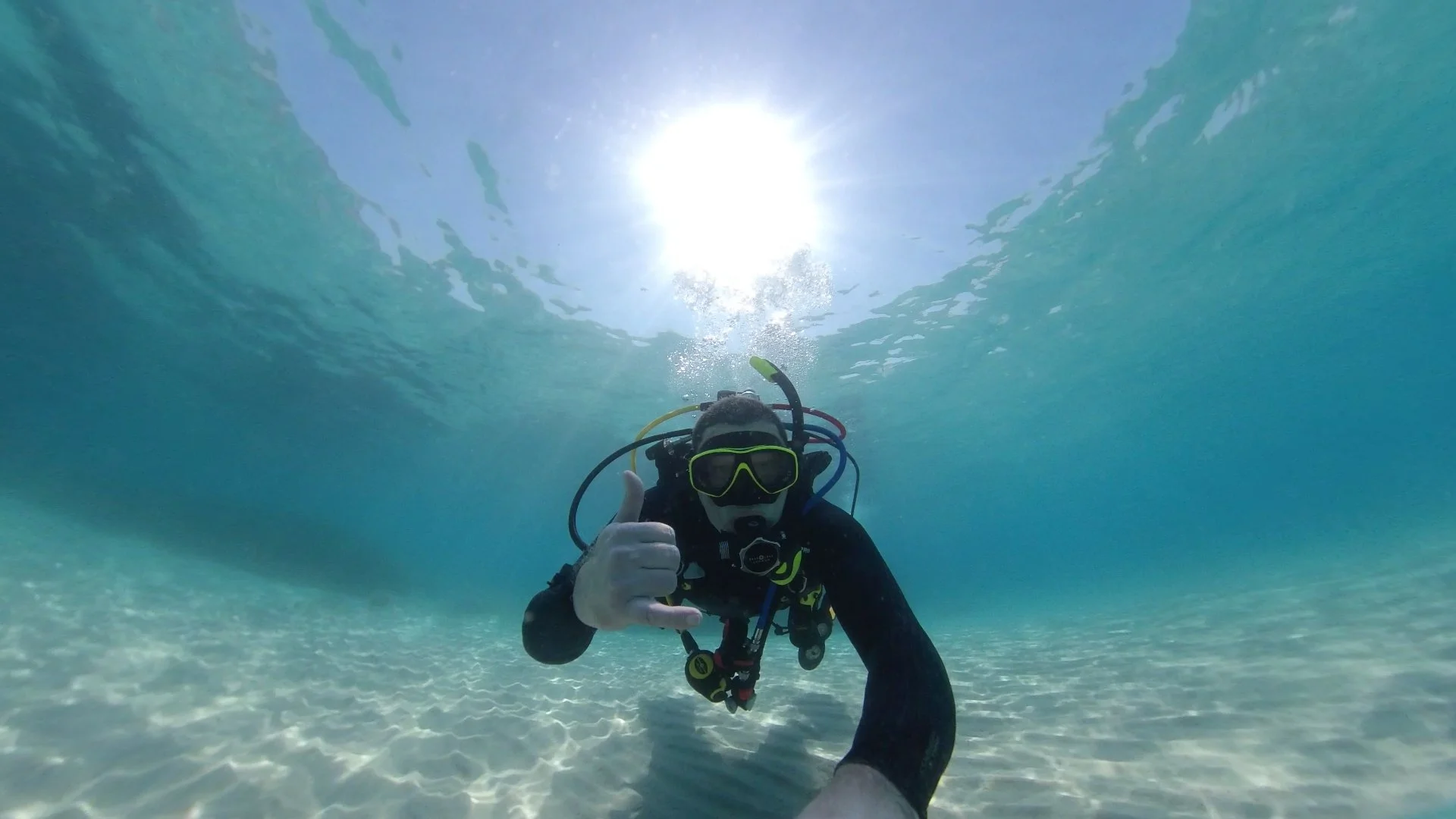 Scuba diver underwater giving a thumbs-up, with sunlight shining through the water surface above.