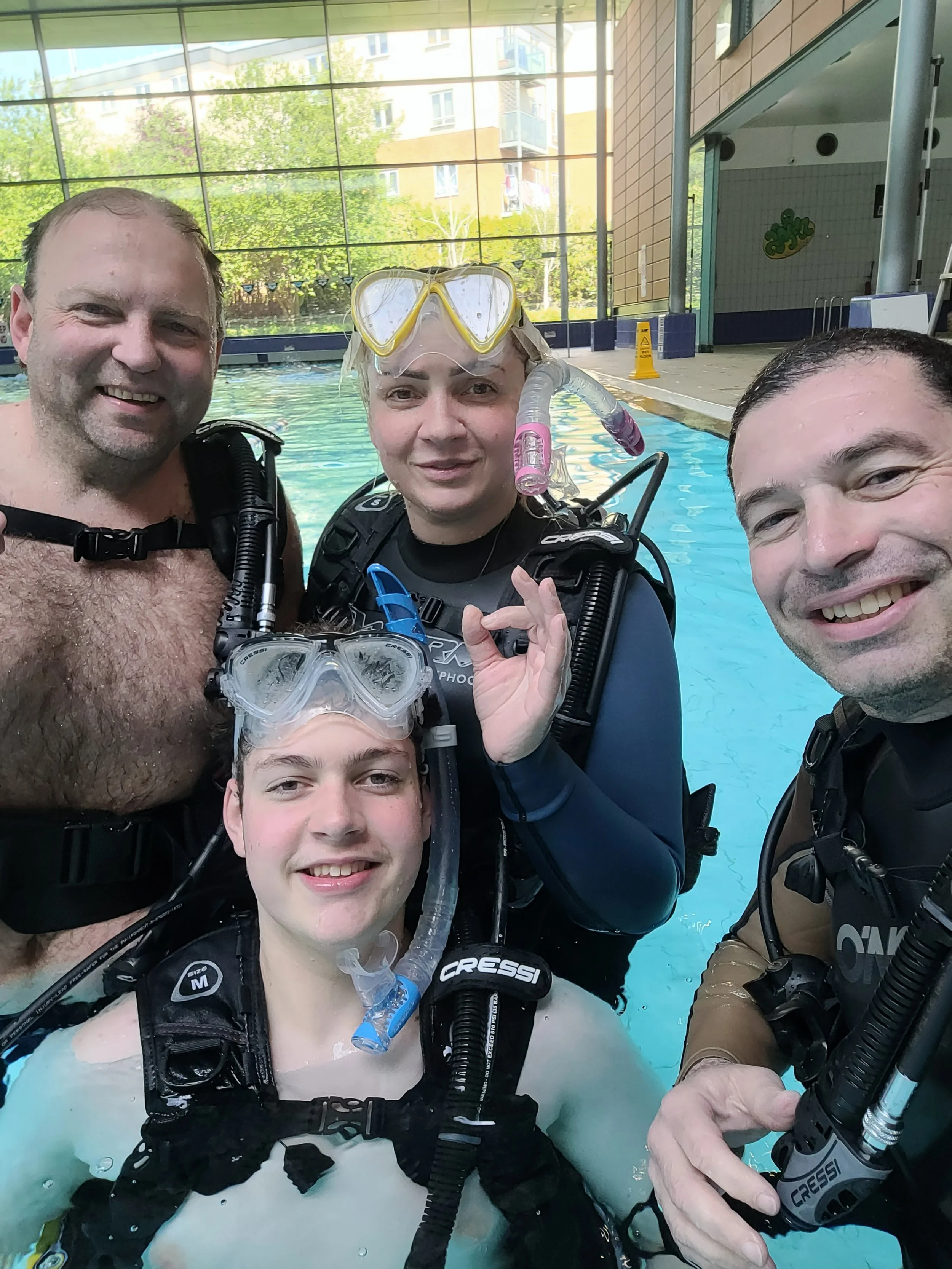 Four people in scuba gear at a swimming pool taking a group photo.