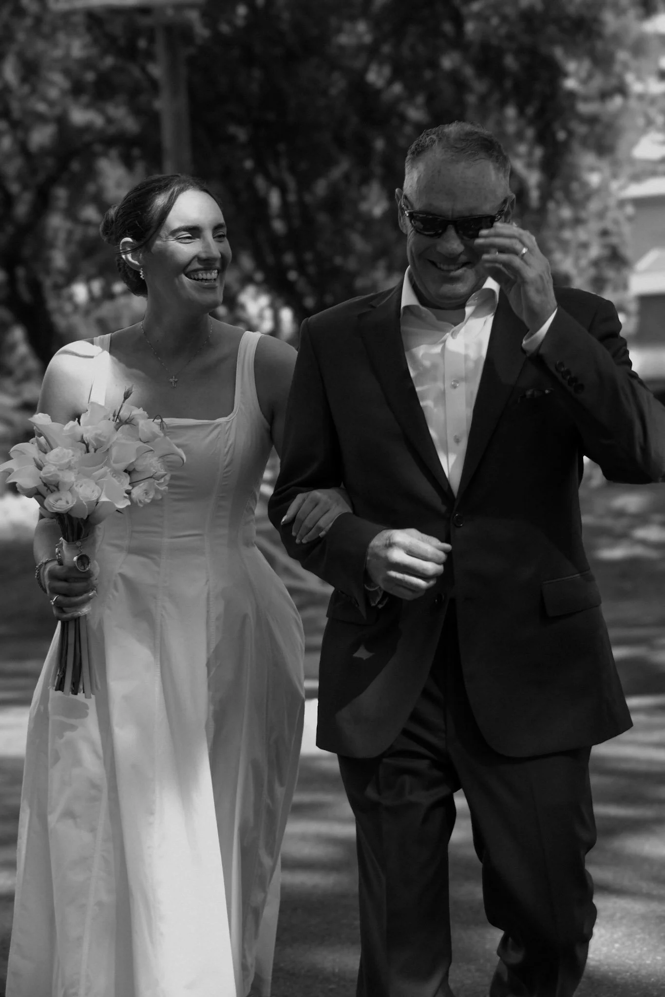 Bride walking arm in arm with a loved one, smiling and laughing together in a candid black and white moment.