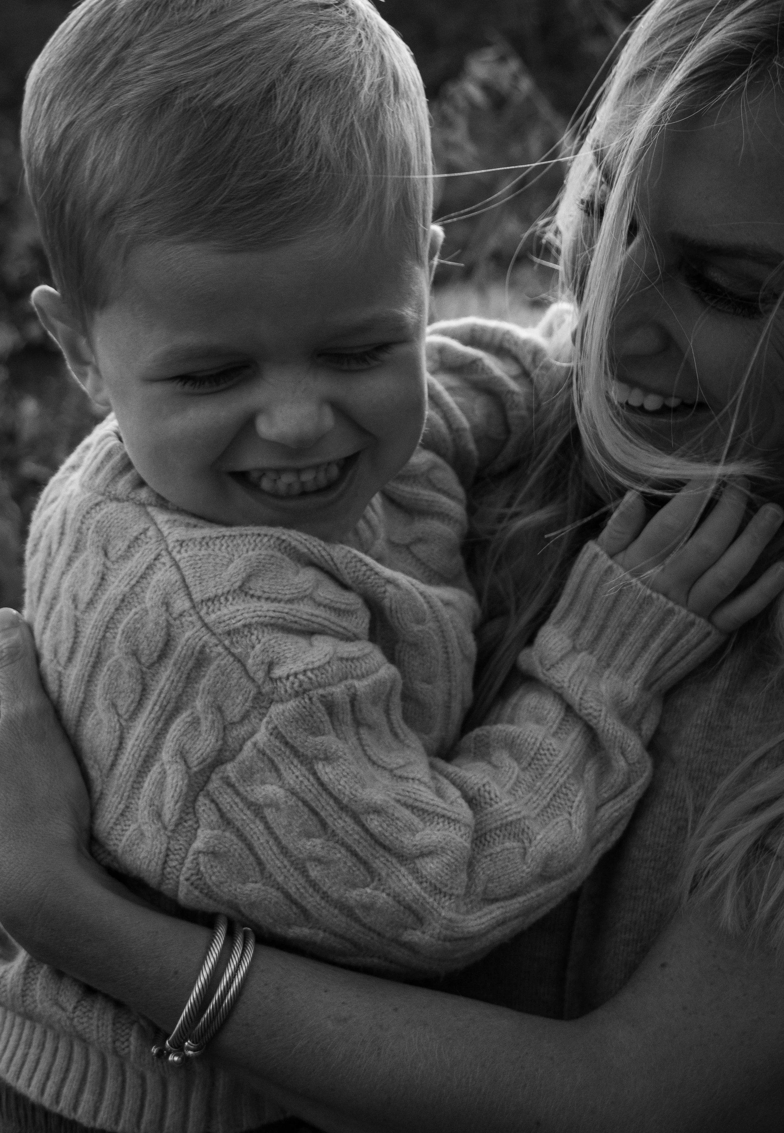 Joyful black and white portrait of a child laughing in someone’s arms, capturing connection and warmth. Motherhood ignited.