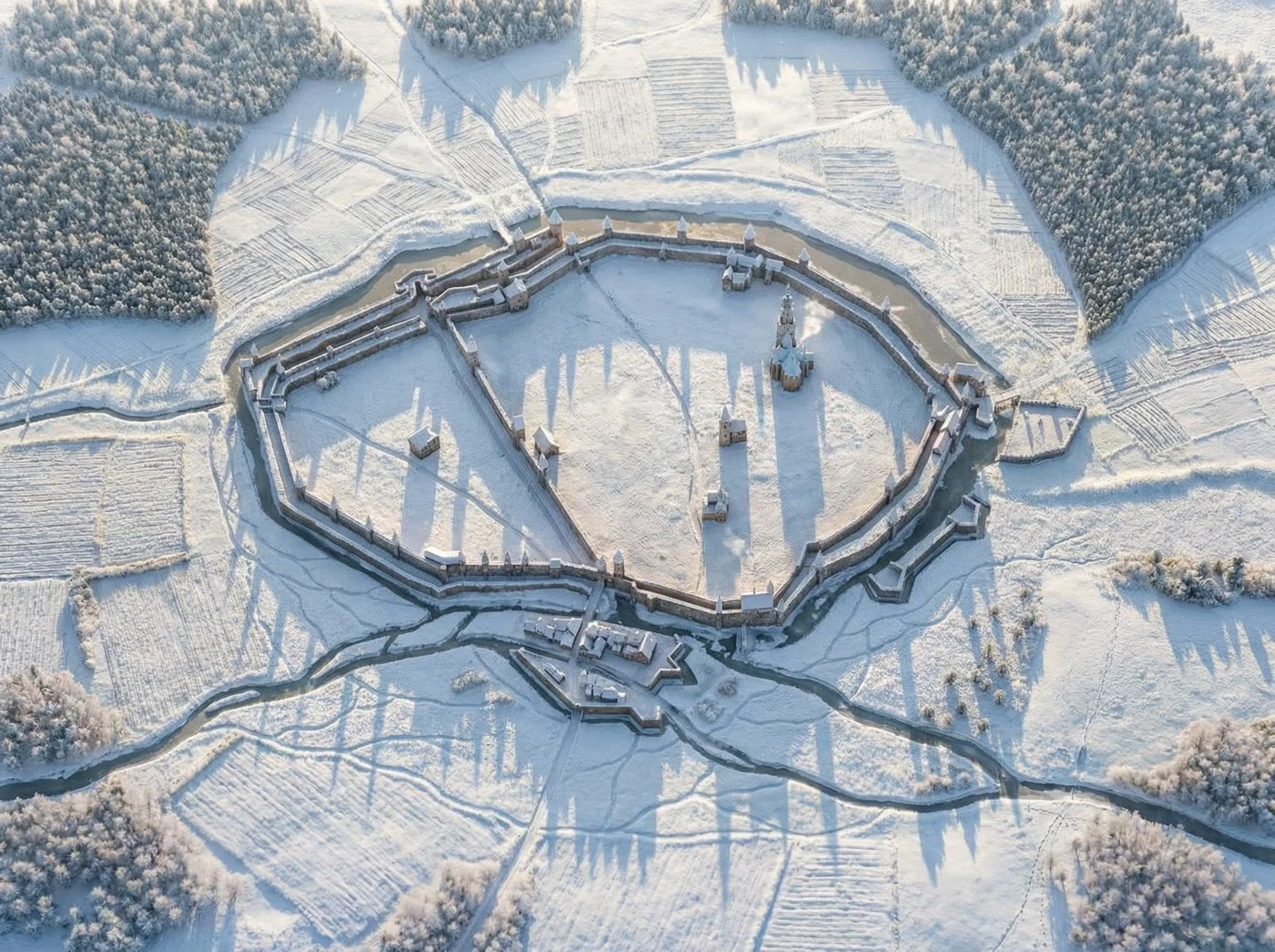 A snowy aerial view of a medieval fortress surrounded by a moat, with snow-covered fields and forests in the background.