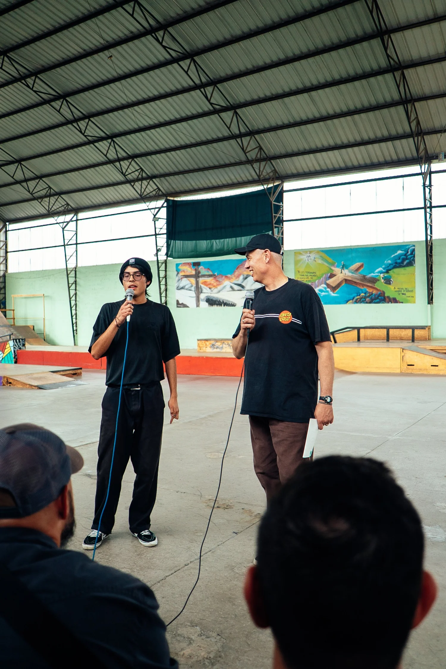 Two leaders speaking into microphones to a group gathered at La Roca.