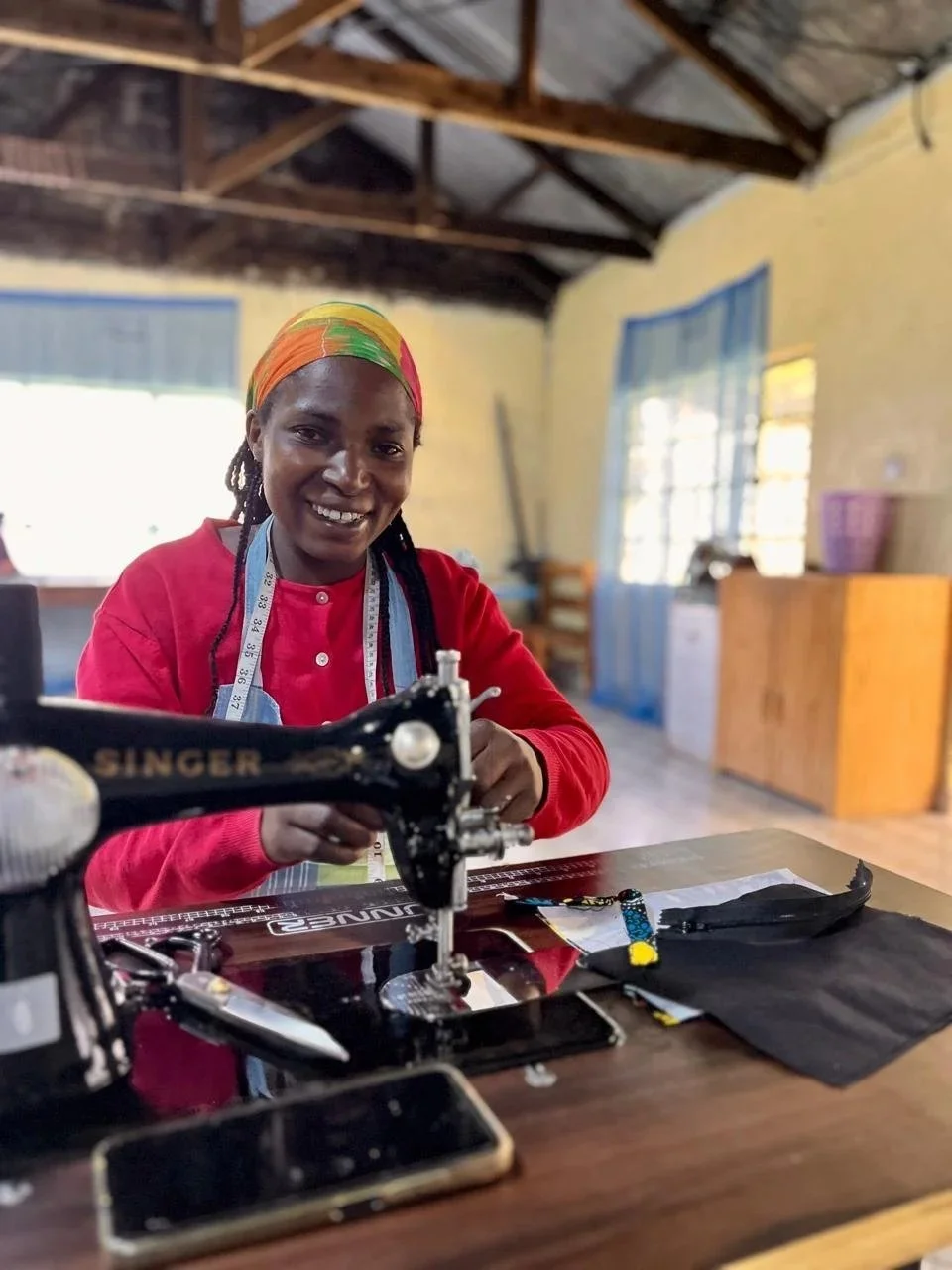 Teresia smiling at a Singer sewing machine in the Threads of Hope workshop in Tumaini, Kenya