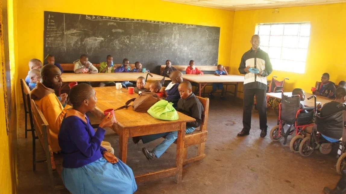 Children and young people, some in wheelchairs, seated at tables in a bright yellow classroom at Matumaini Rehabilitation Centre
