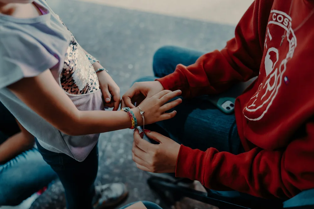 A young leader fastens a handmade bracelet on a girl's wrist at La Roca.