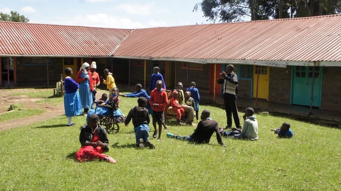 Children, young people and caregivers, some in wheelchairs, gathered on the lawn in front of the red-roofed buildings of Matumaini Rehabilitation Centre