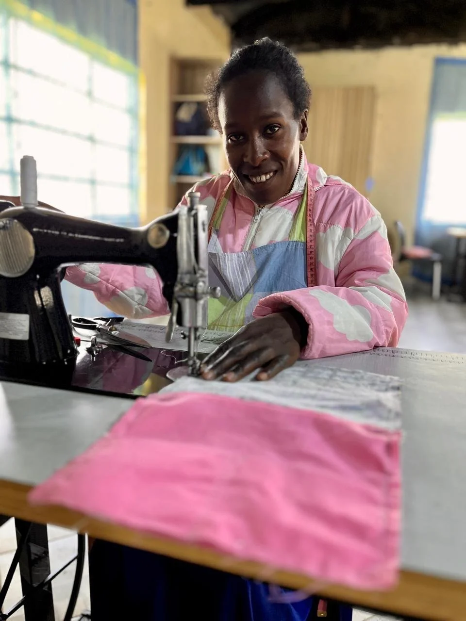 Susan smiling as she works at a Singer sewing machine in the Threads of Hope workshop