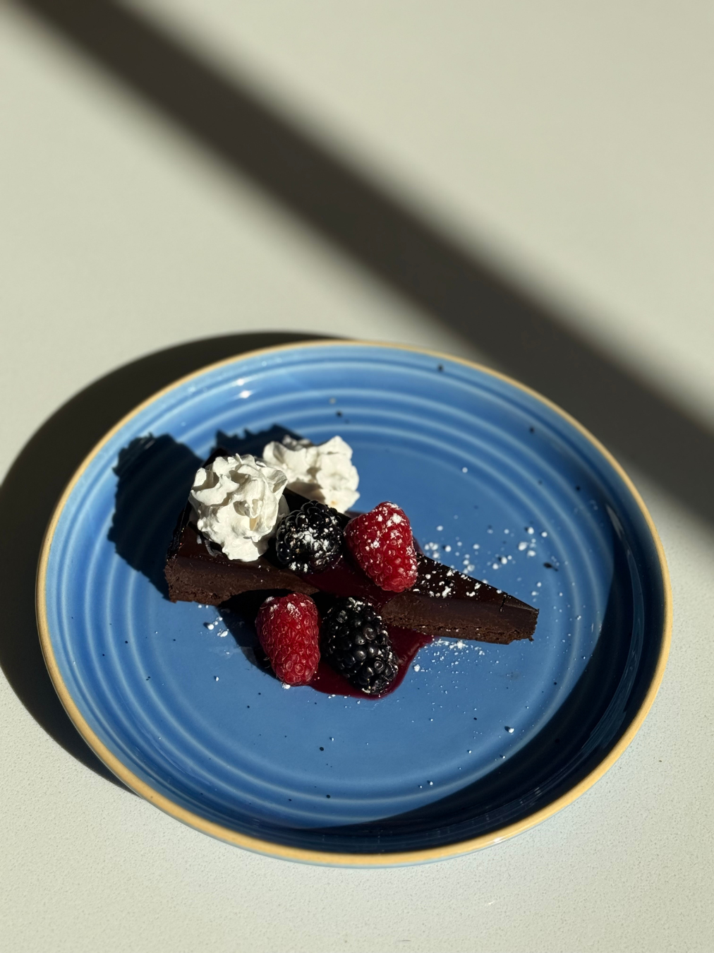 Rich chocolate torte topped with fresh berries and a dusting of powdered sugar, served on a blue plate