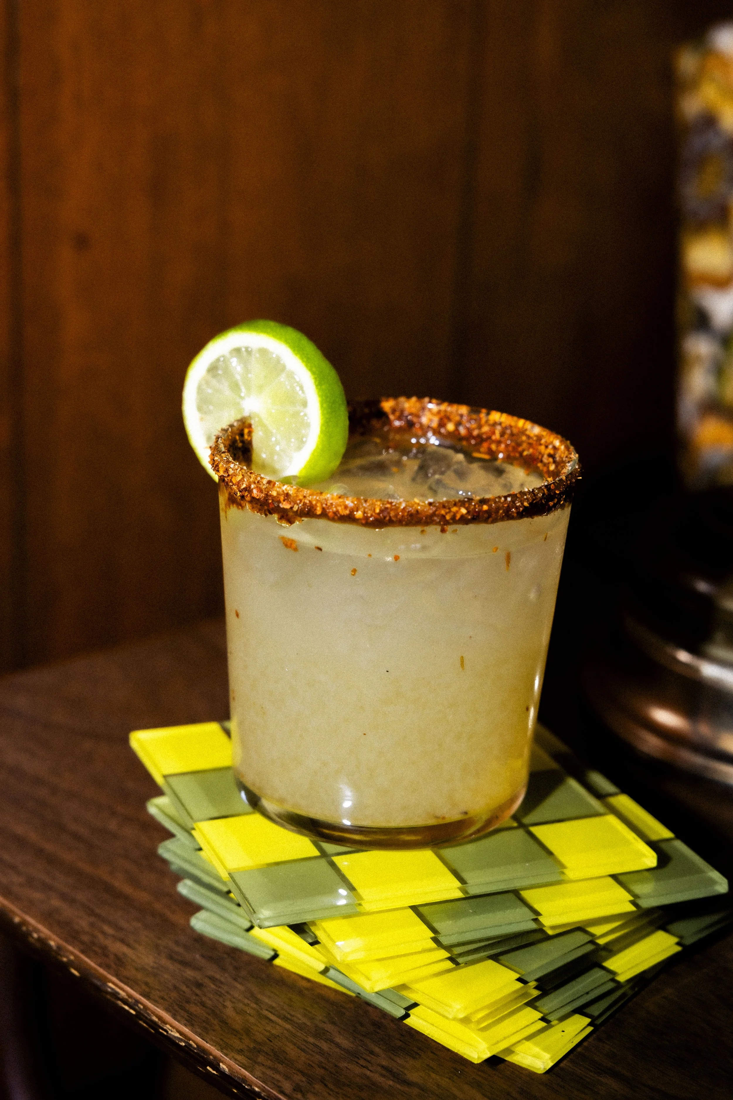 A cocktail glass with a pinkish frothy drink garnished with a pineapple slice, placed on a wooden surface next to two empty wine glasses.