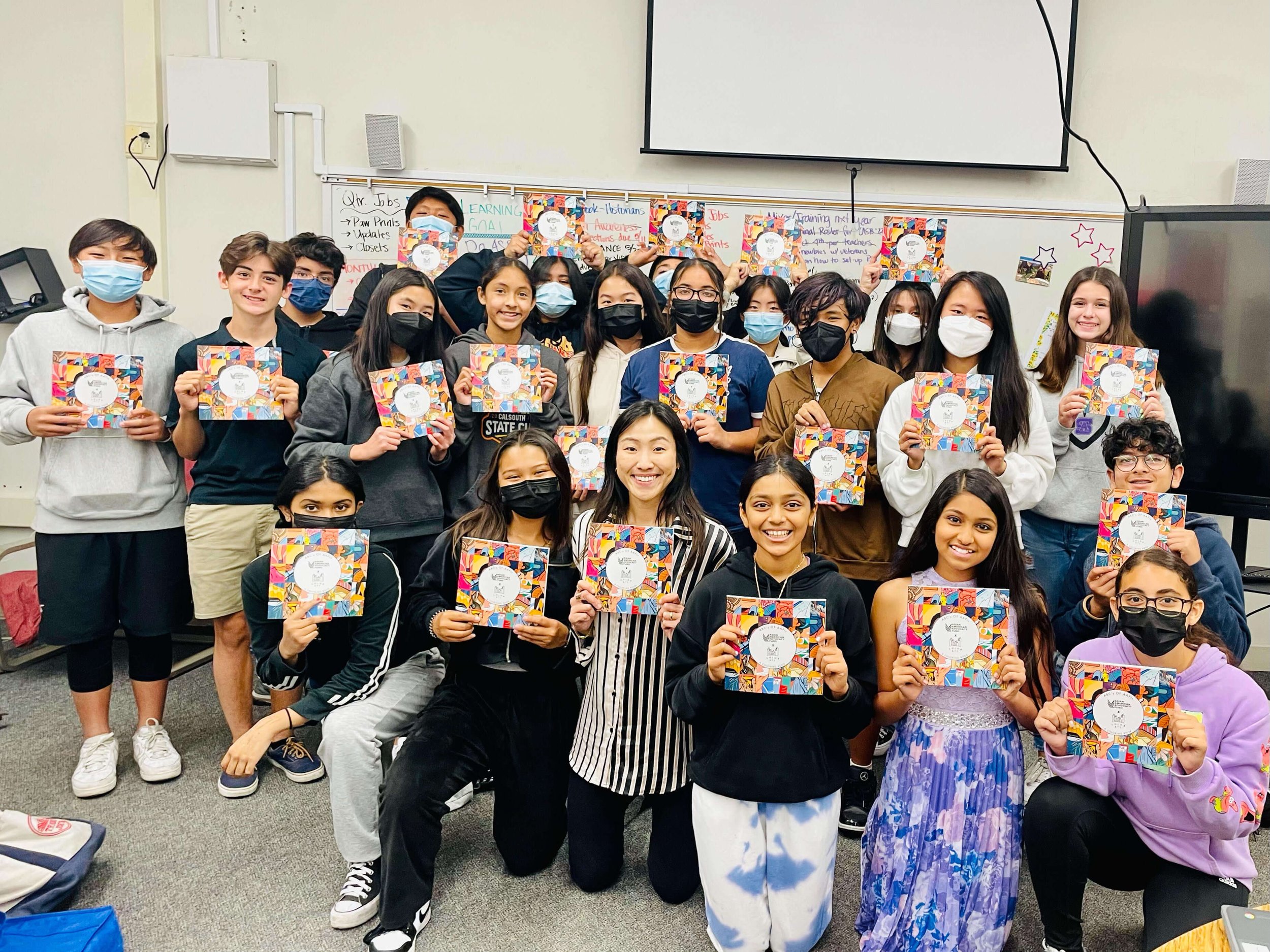  Classroom full of smiling students (many of them Asian) holding up The ABCs of AAPIs coloring book 