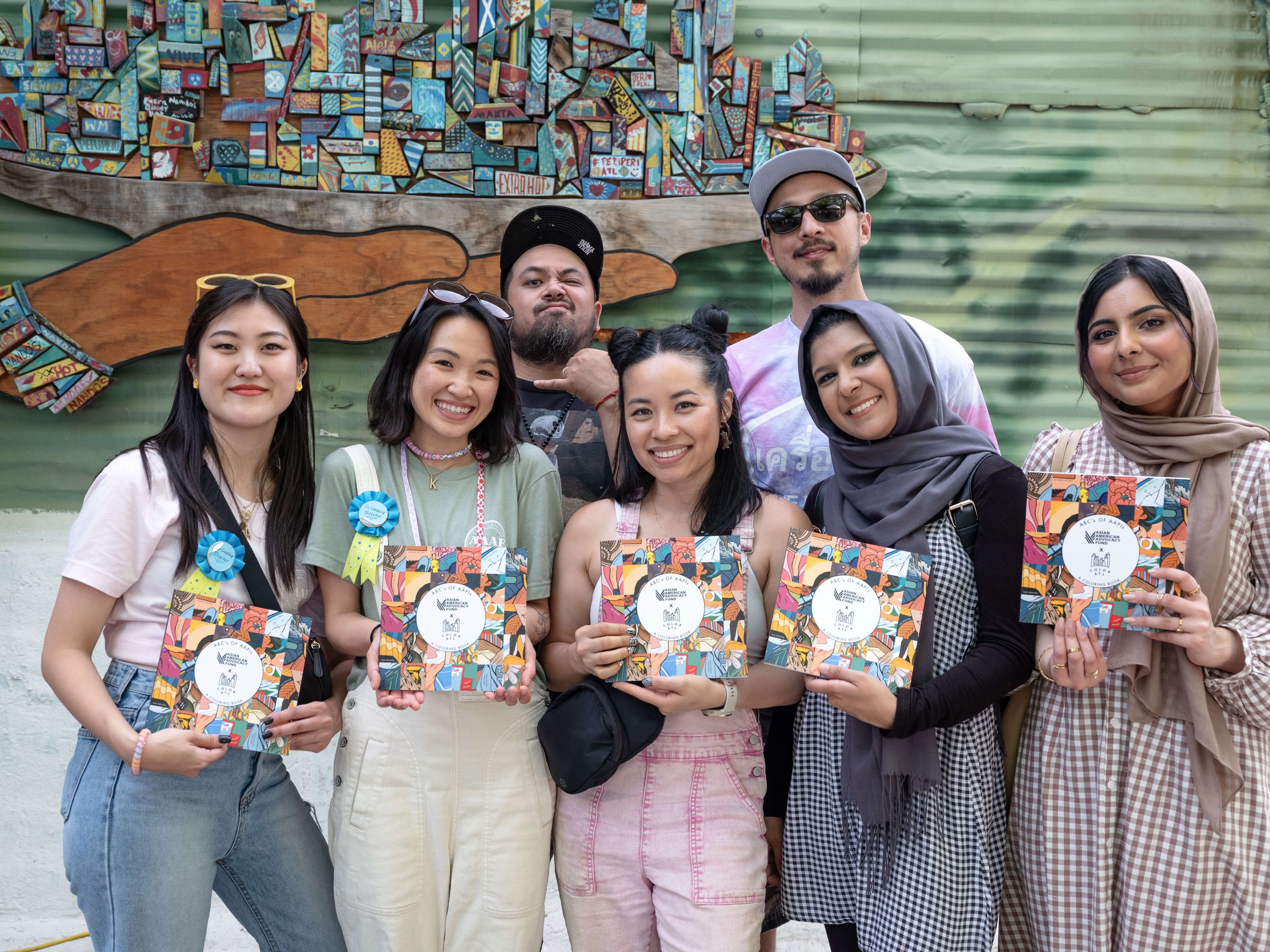  Co-creative directors Arah Kang and Kavi Vu with a group of artists proudly holding their coloring books up 