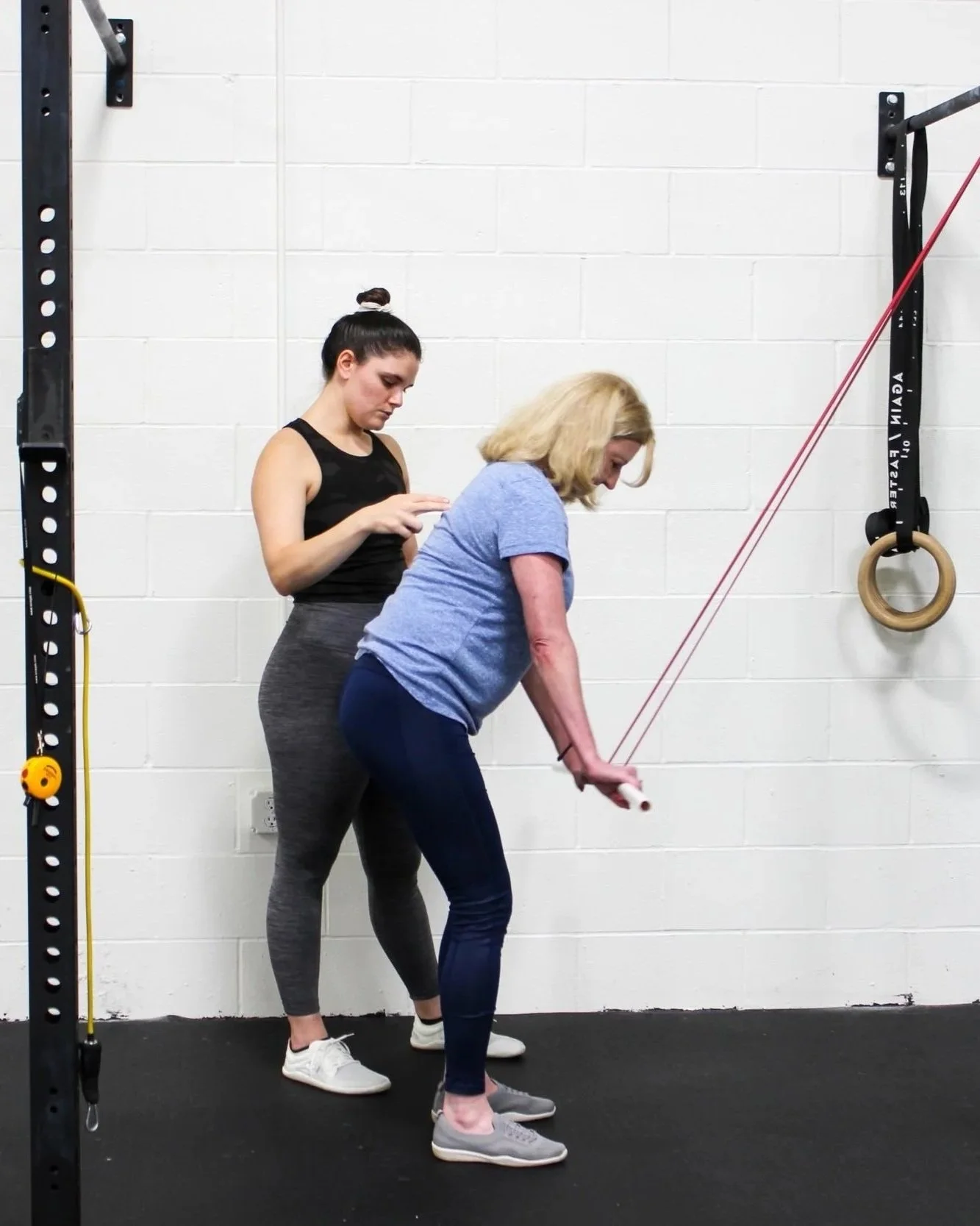 A young woman assisting an older woman with a tricep extension exercise using a resistance band attached to the wall.