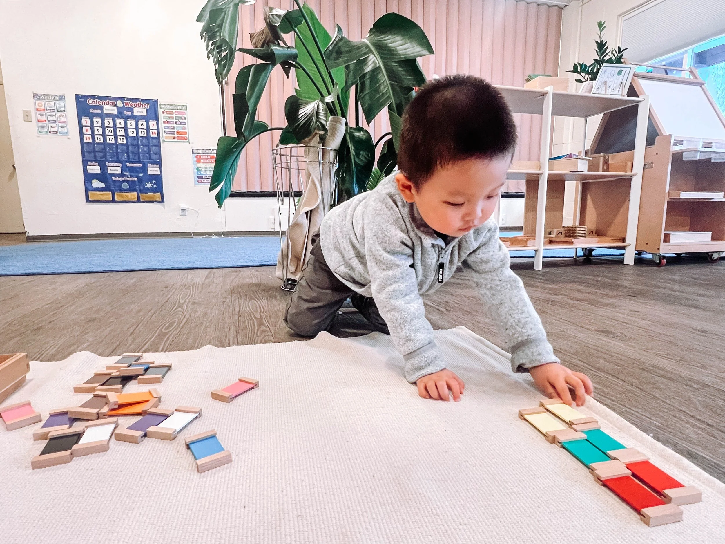 Young child kneeling on carpet playing with colorful building blocks in a classroom.