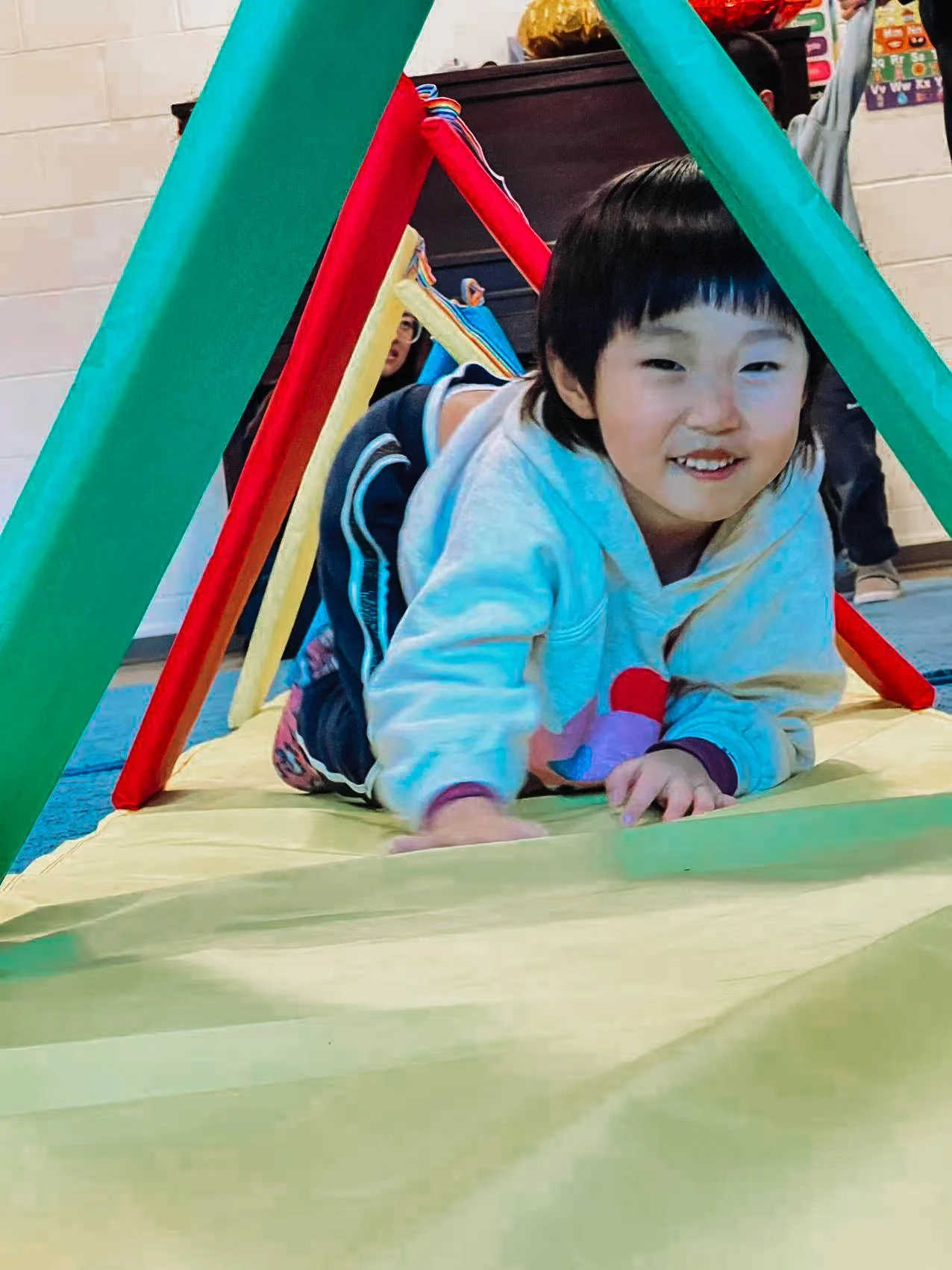Child crawling through a colorful play tent in a classroom
