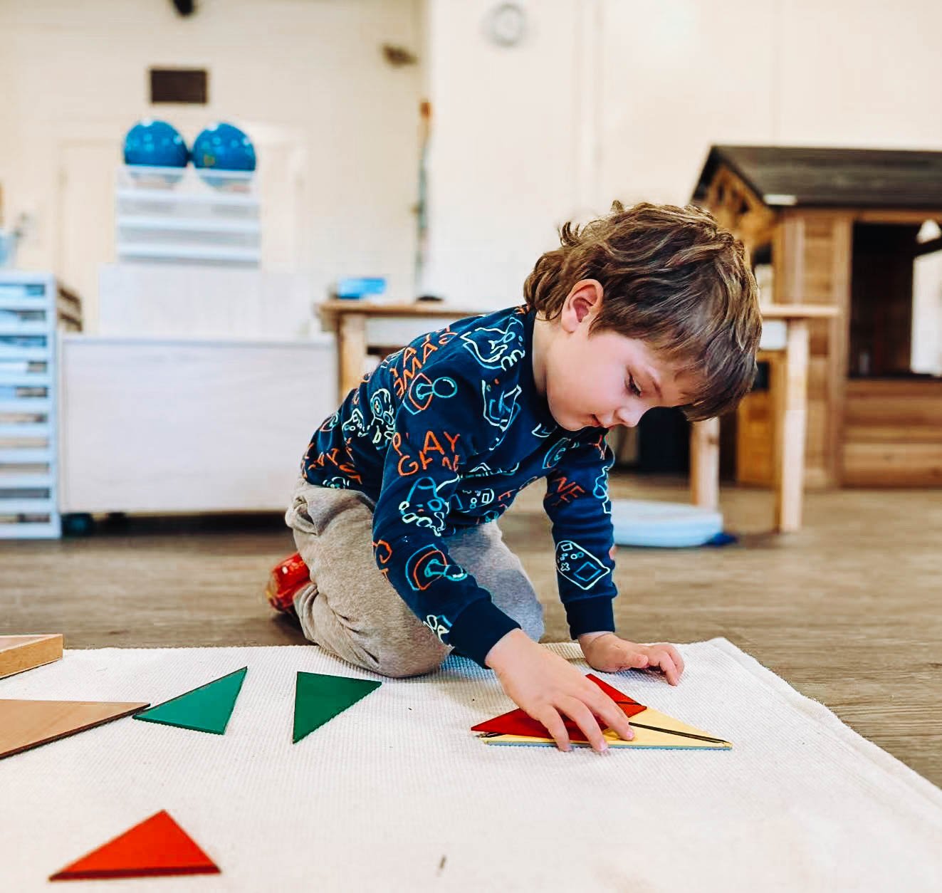 A young boy playing with geometric puzzle pieces on a carpeted floor in a playroom.
