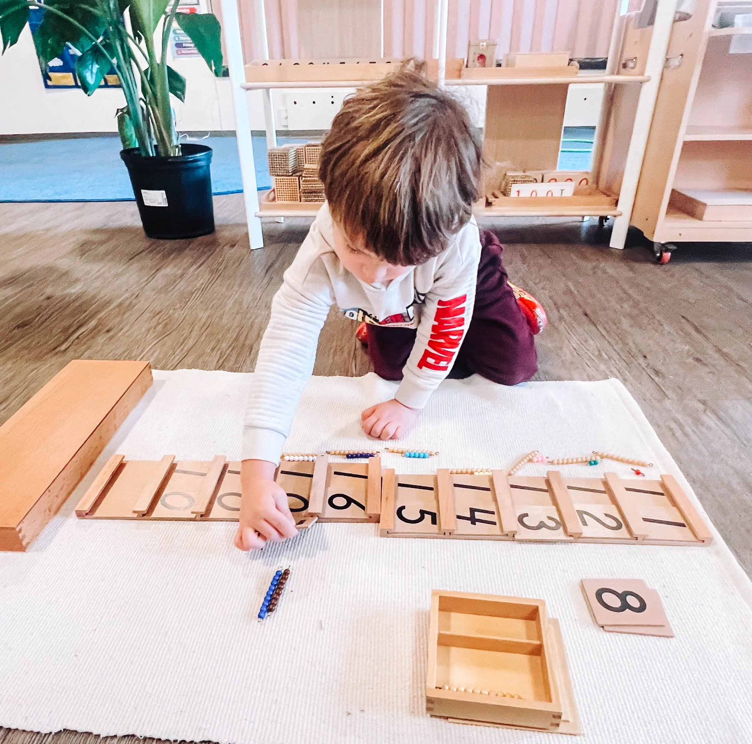 Child engaging with number sequencing activity on a white cloth in a classroom.