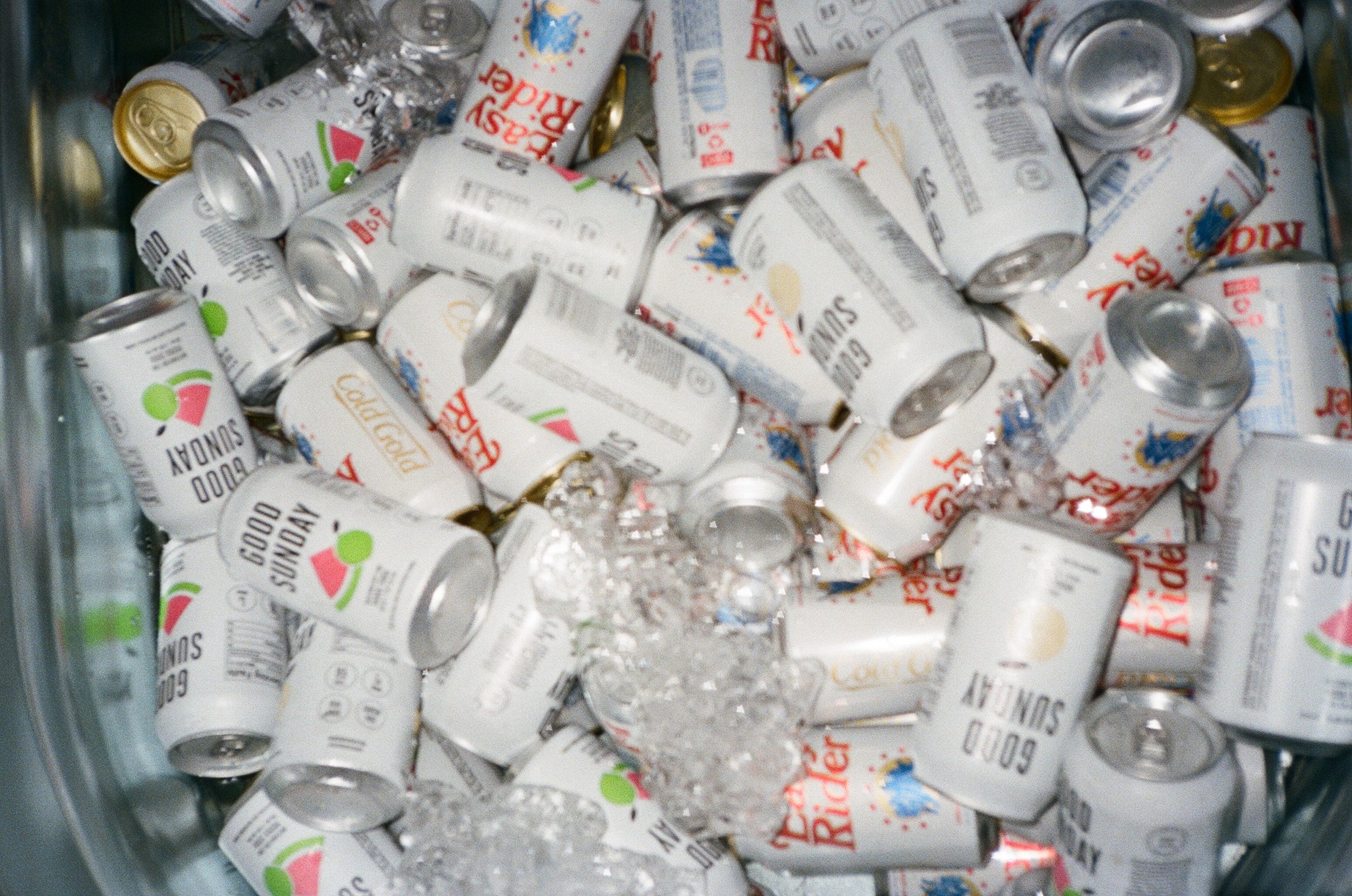 Assorted beverage cans with various labels in a cooler with ice.