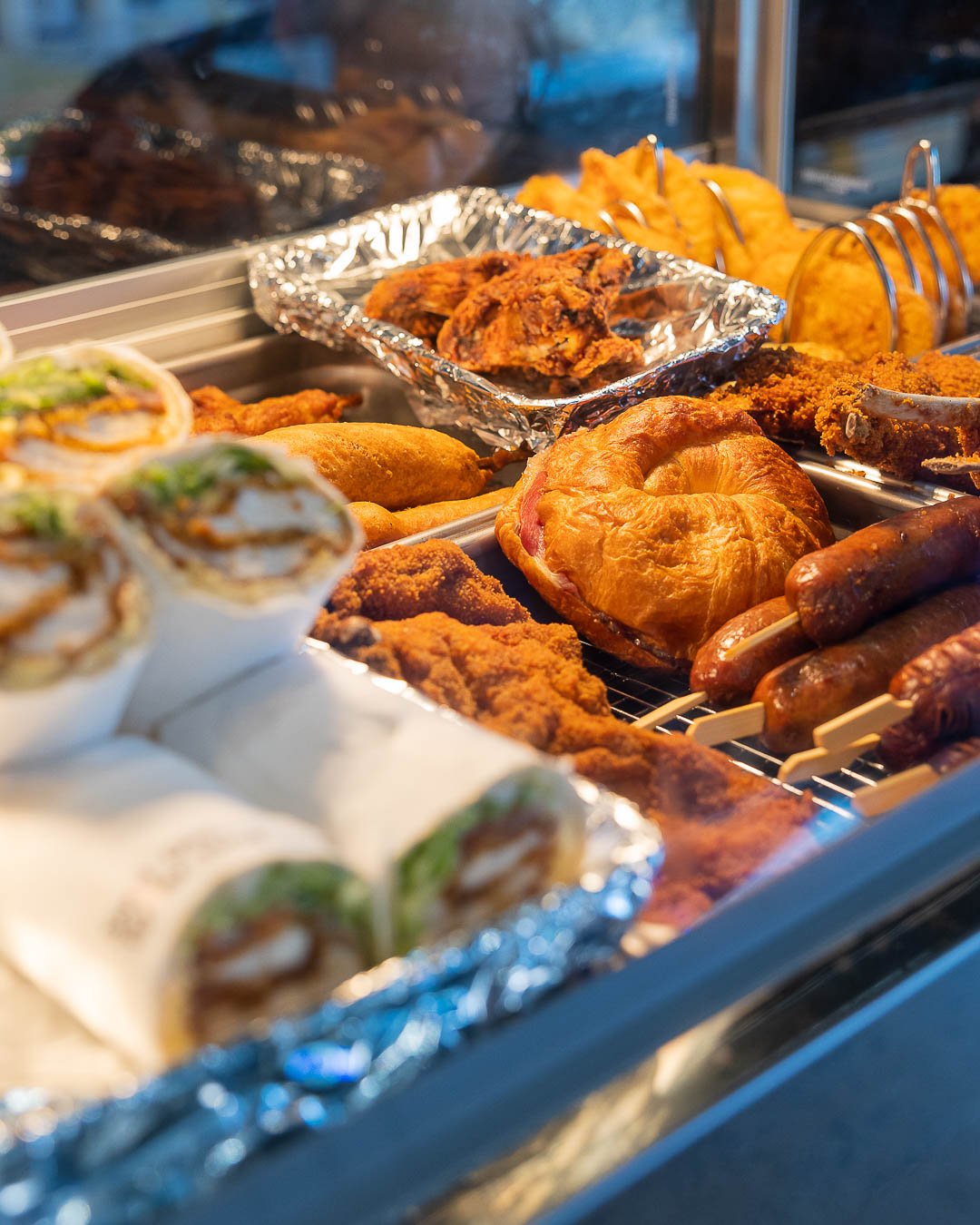 Hot food in the Bain-marie including ham and cheese croissant, dagwood dog, chicken wings, crumbed lamb cutlets and scallops