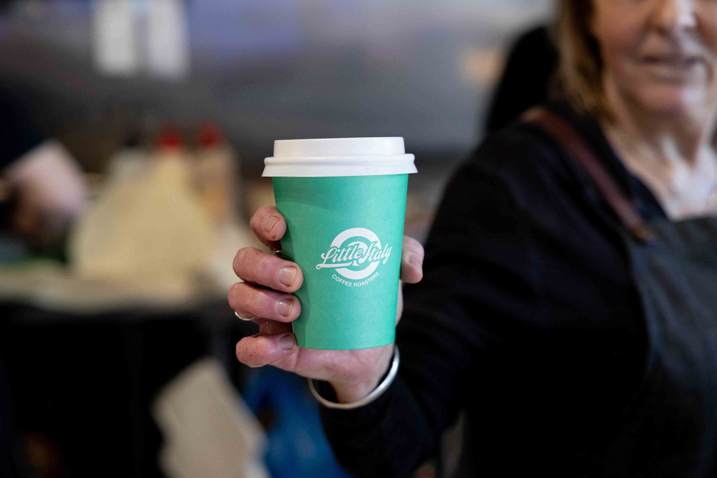 Hand holding out a mint green little italy coffee roasters takeaway cup