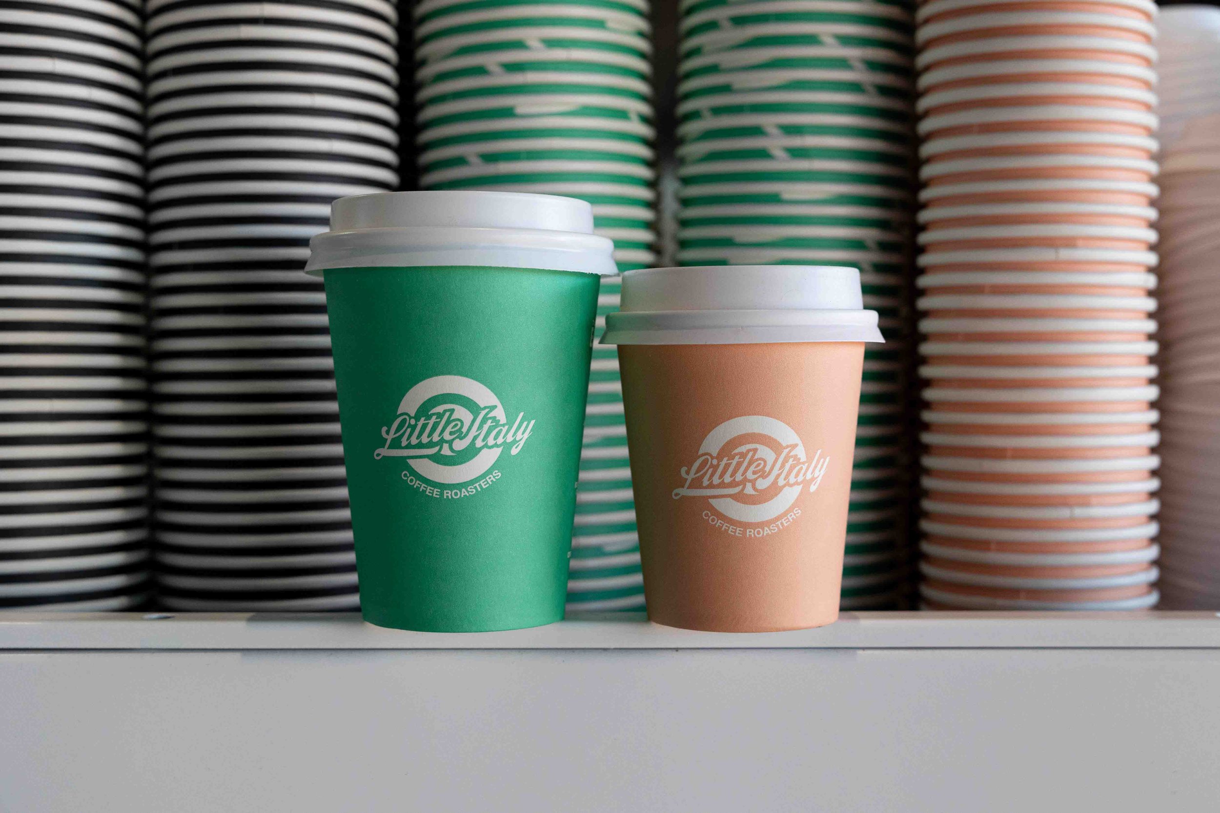 Mint green and peach coloured takeaway coffee cups with little italy coffee roasters logo on them sitting on top of the coffee machine