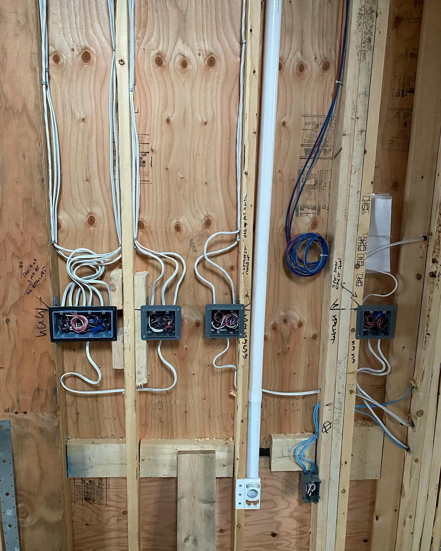 Electrical wiring and outlets installed on wooden wall studs, with some wiring organized in boxes and conduit.