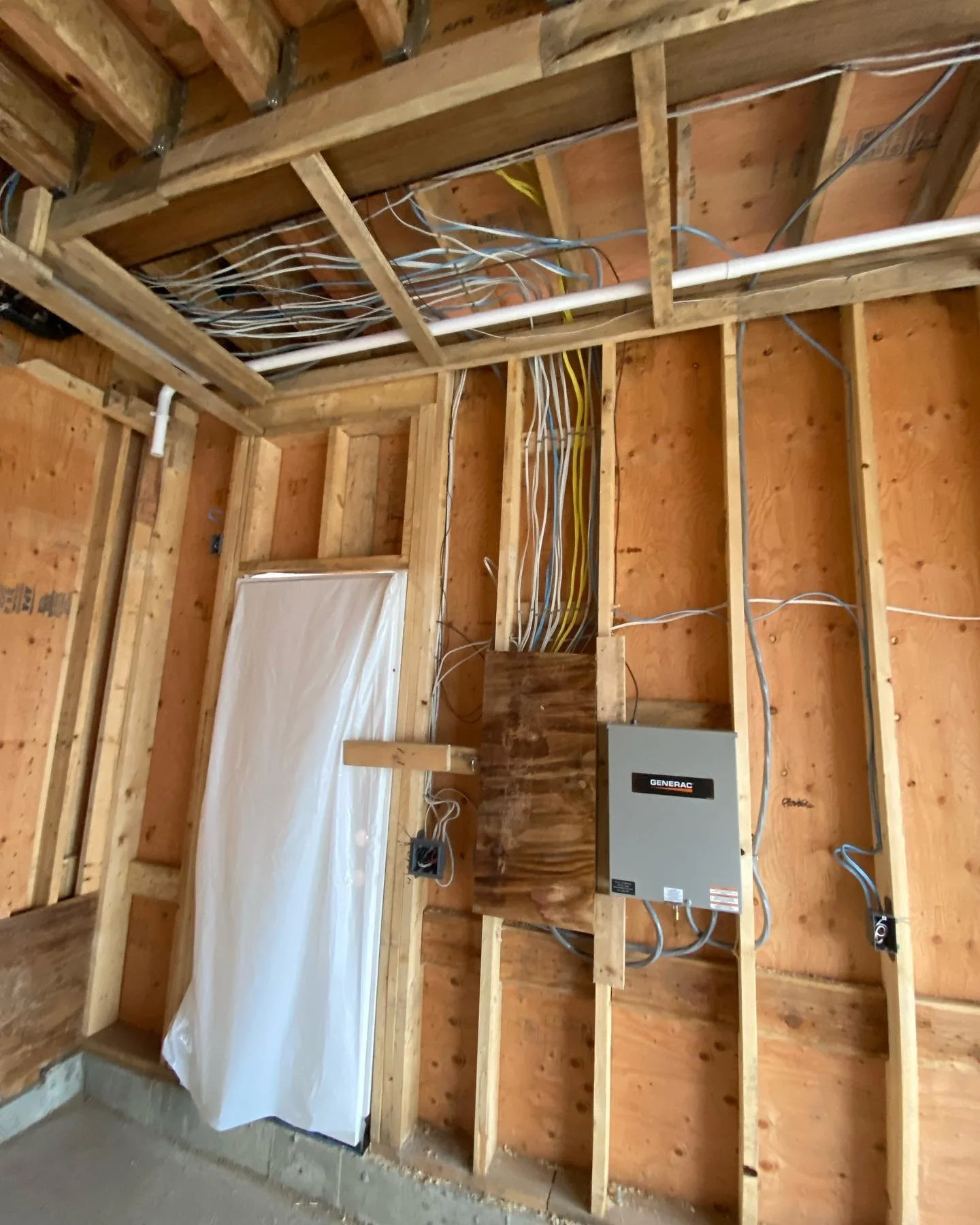Construction of a building's interior wall with exposed wooden framing, electrical wiring, and a gray electrical panel labeled 'Generac'.