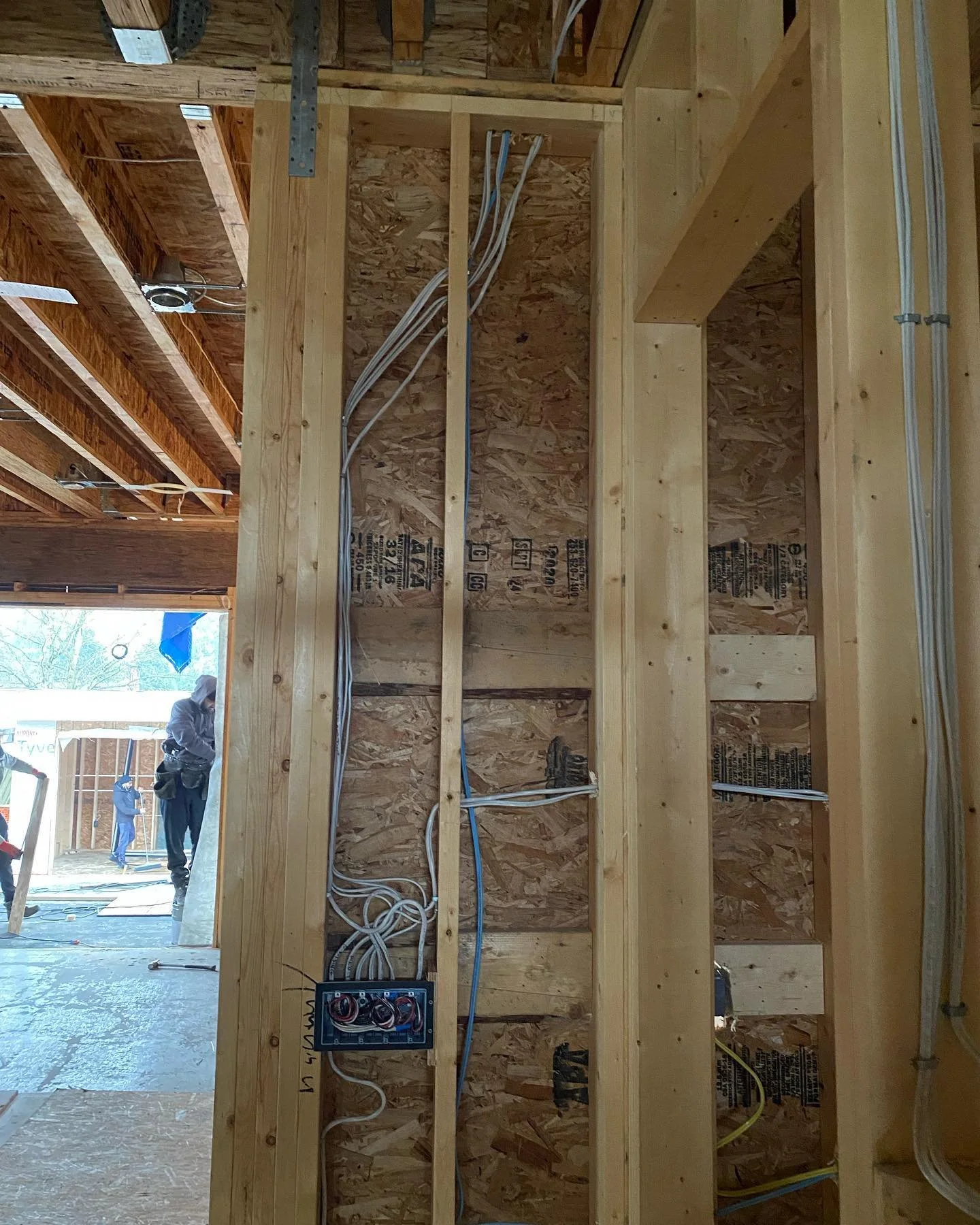 The image shows the interior framing of a building under construction, with electrical wiring installed in the wall studs and an electrical junction box mounted on the wood.